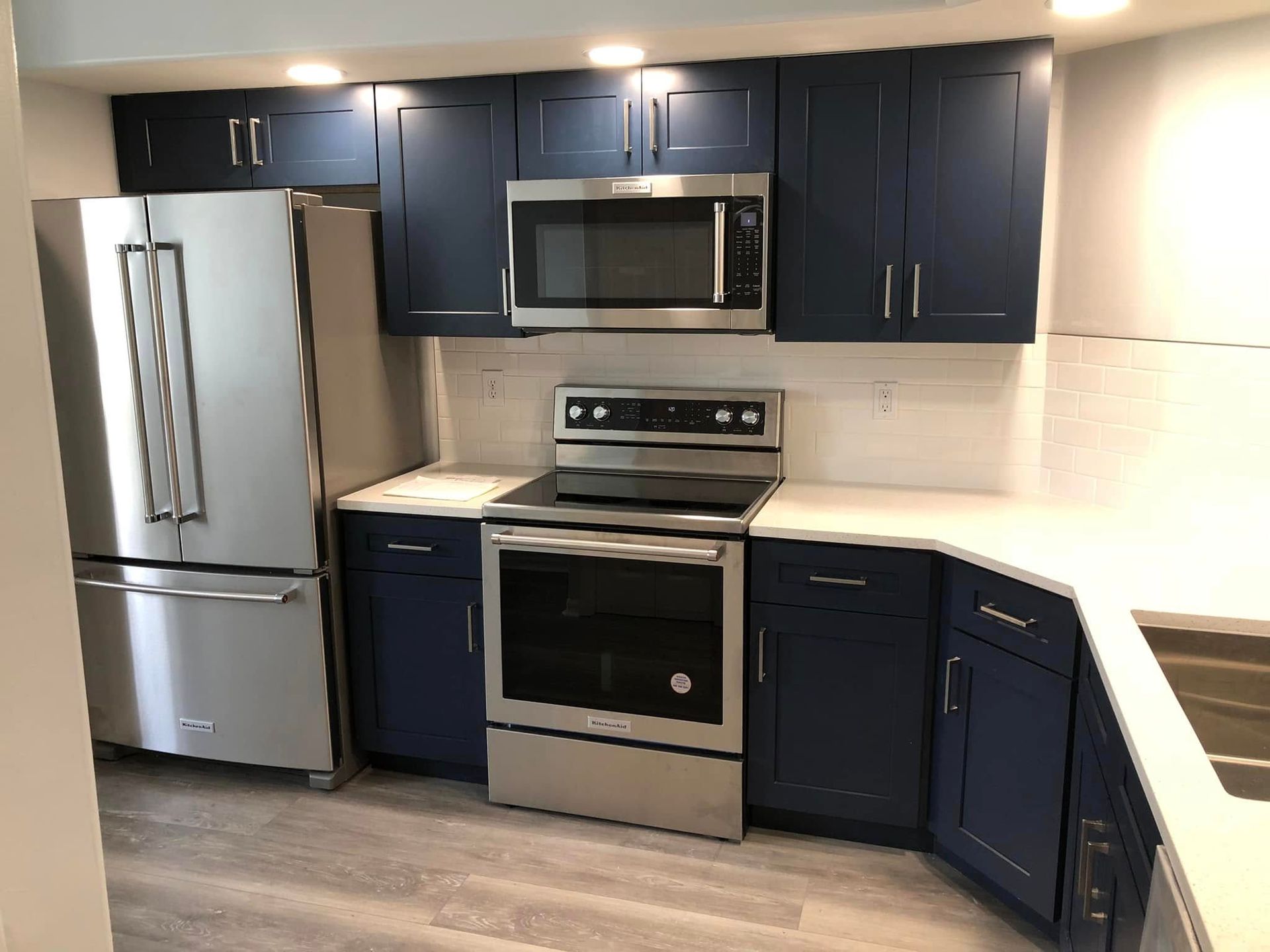 Modern kitchen with stainless steel appliances, dark blue cabinets, and white countertops