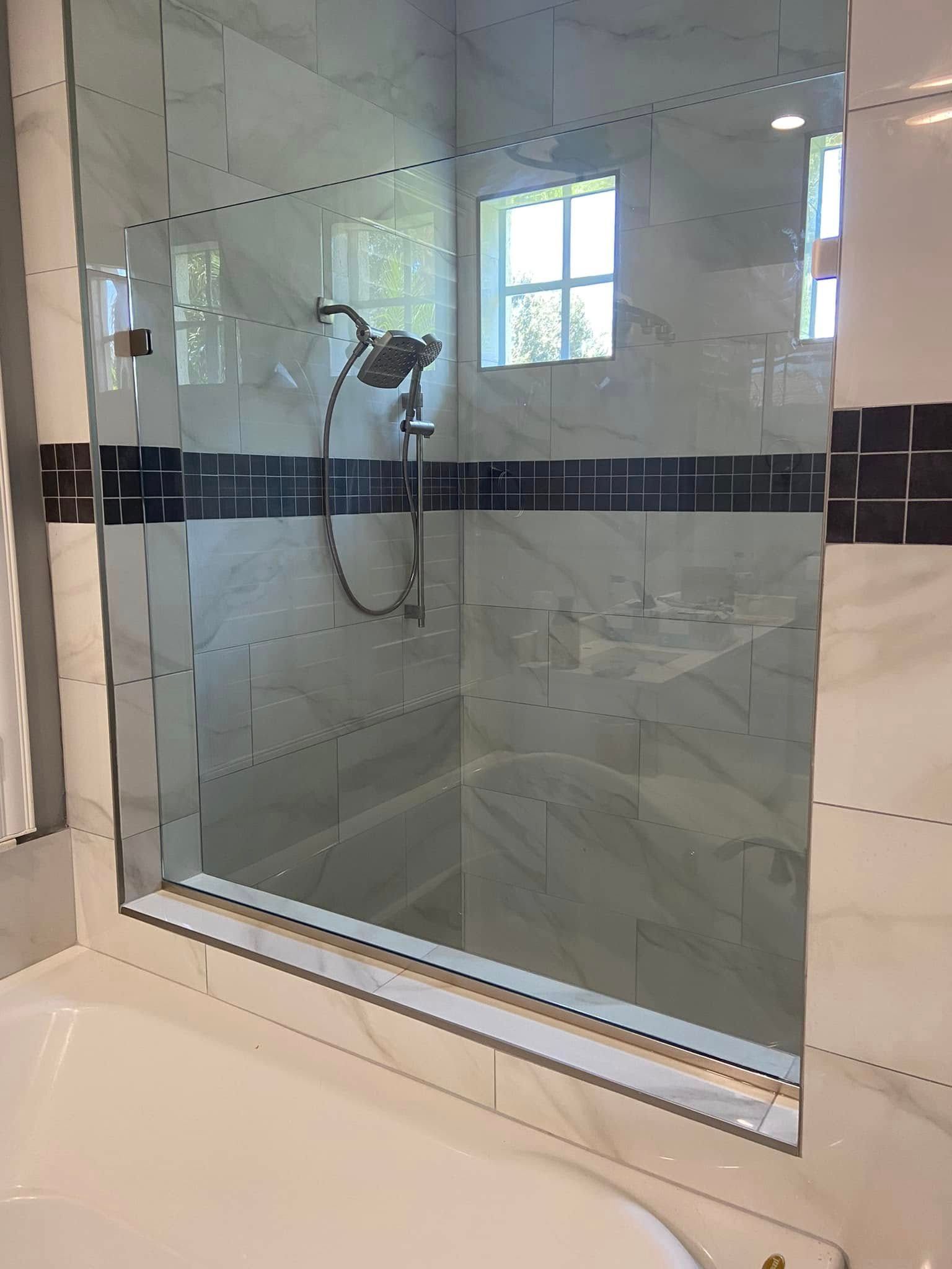 Bathroom shower seen through a glass partition, with tiled walls and a showerhead visible inside.