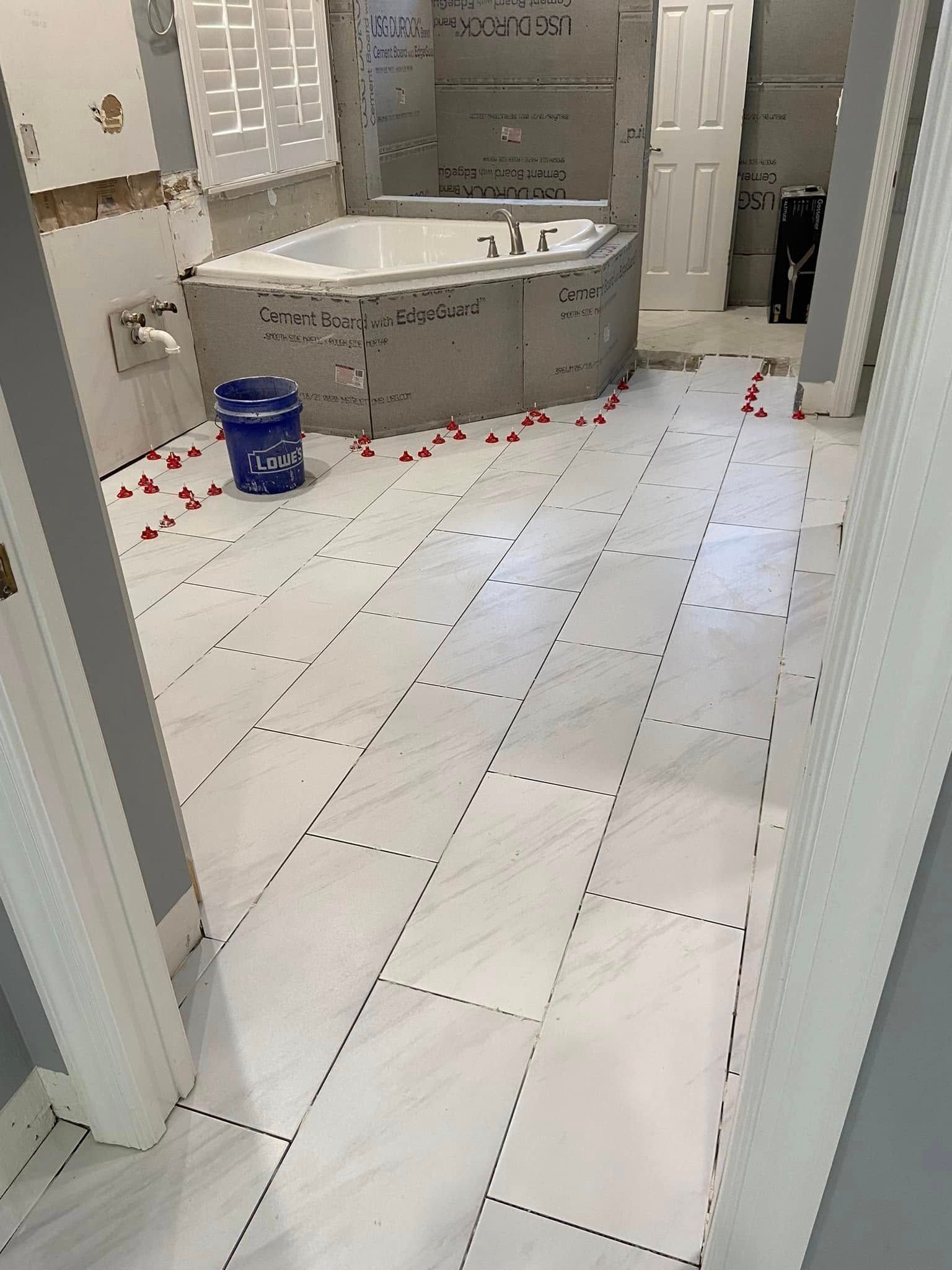 Bathroom with white tiled floor, gray marble tub, and a blue bucket near scattered red petals.