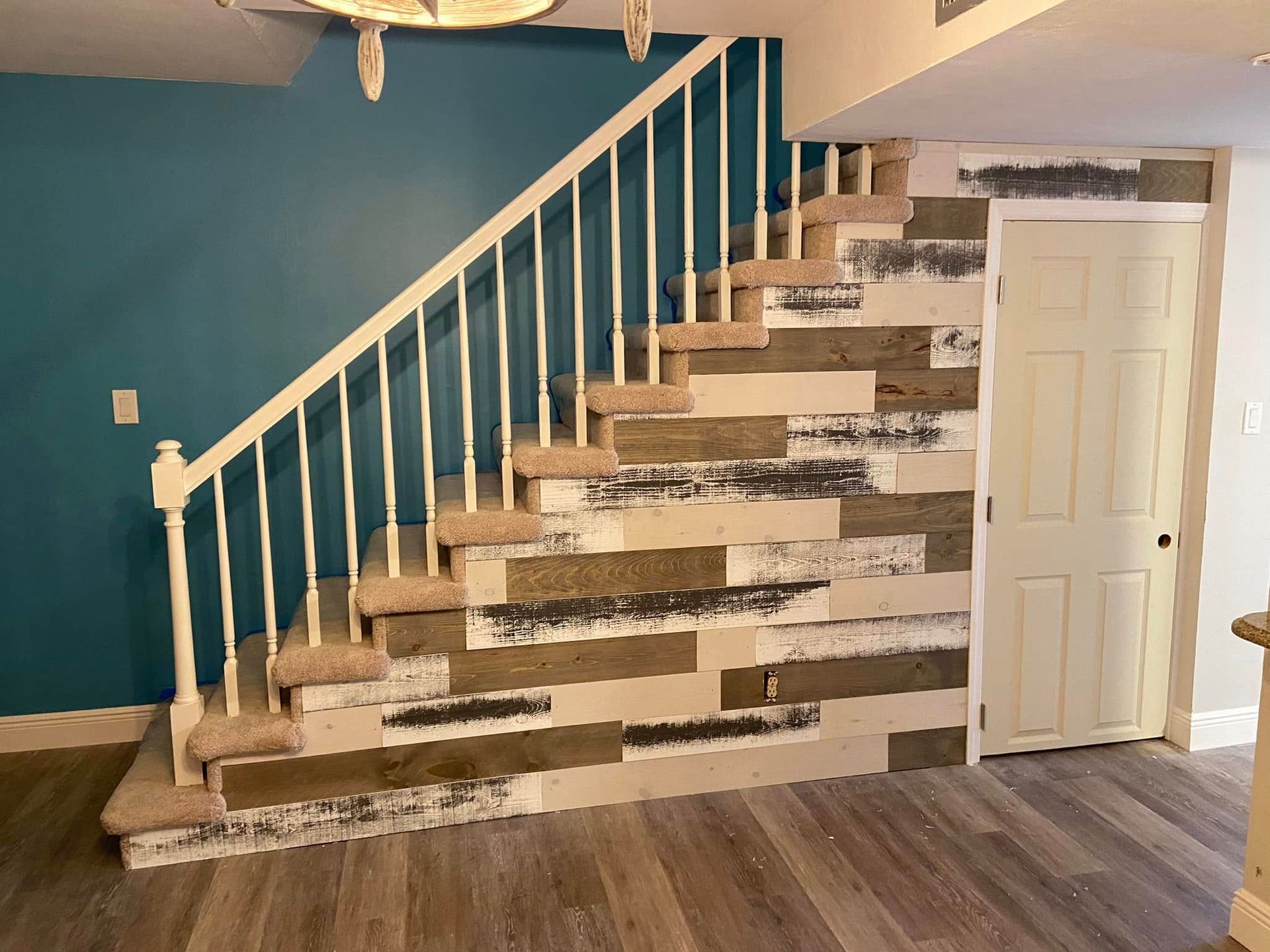 Interior staircase with blue wall, white railing, wood floor, and a paneled door beneath the stairs
