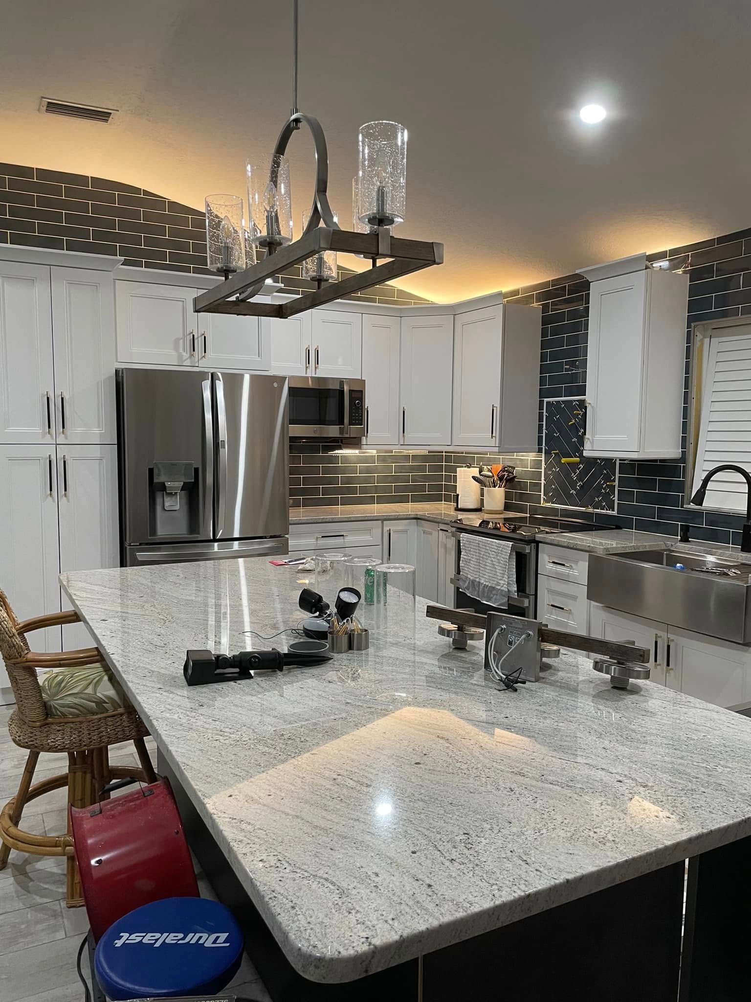 Modern kitchen with white cabinets, stainless steel appliances, and a large granite island with pendant lights.