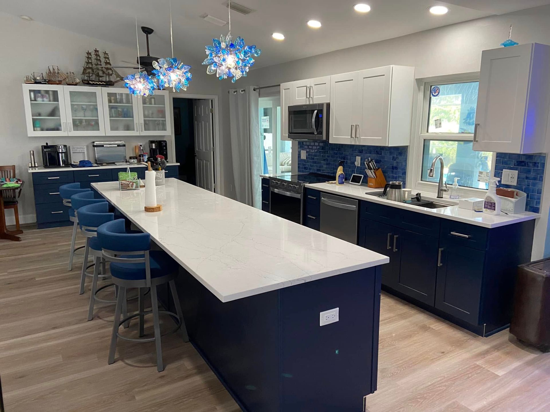 Modern kitchen with a long white island, navy cabinets, blue pendant lights, and stainless appliances