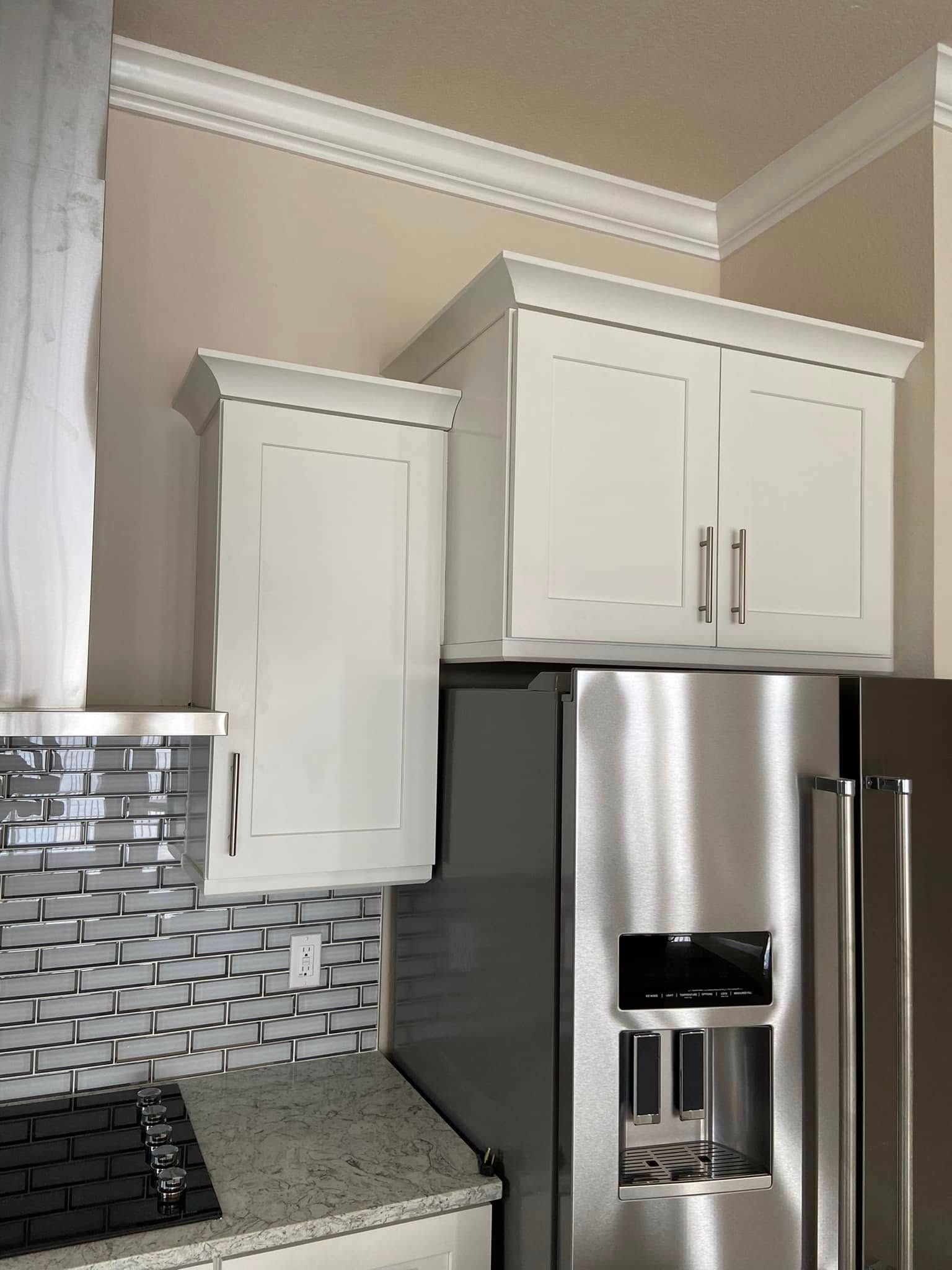 Kitchen cabinets above a stainless steel refrigerator with mosaic tile backsplash and beige walls
