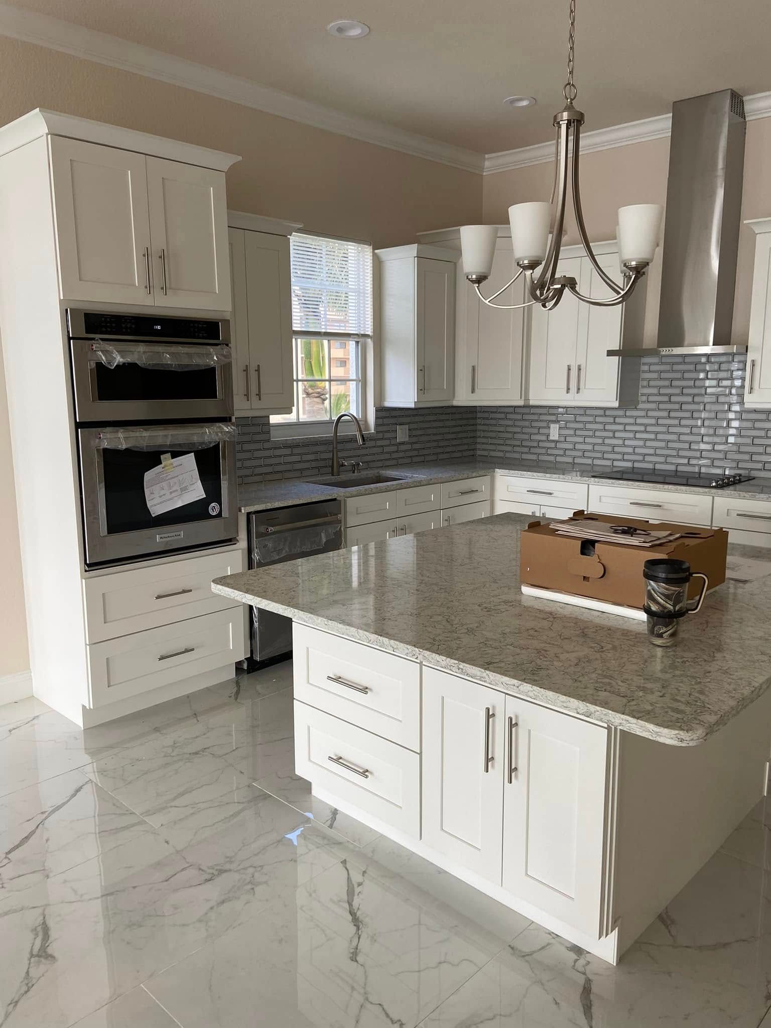 Modern white kitchen with gray countertops, tile backsplash, island, and built-in double oven