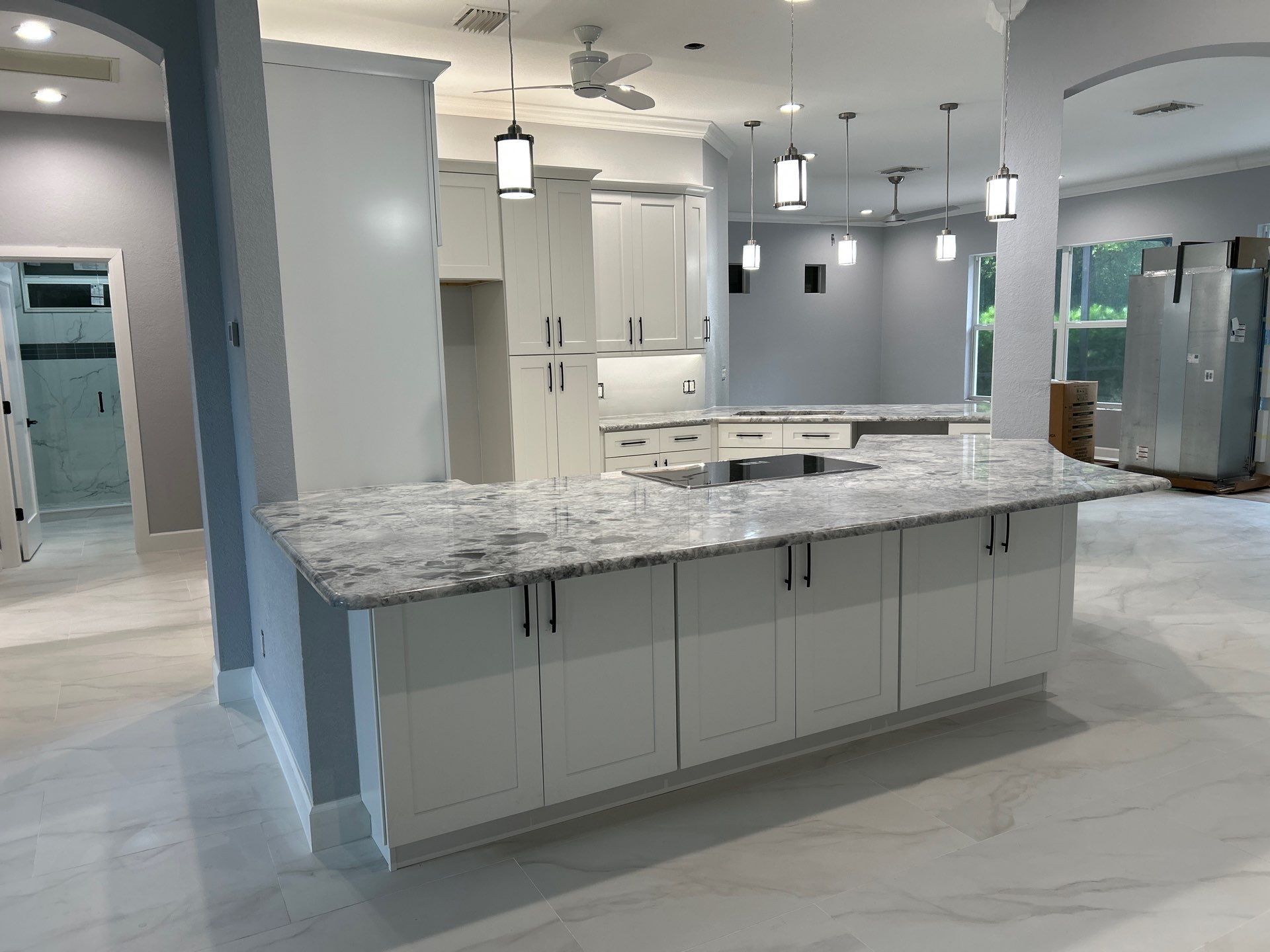 Modern kitchen with gray cabinets, marble island, white tile floor, and pendant lights