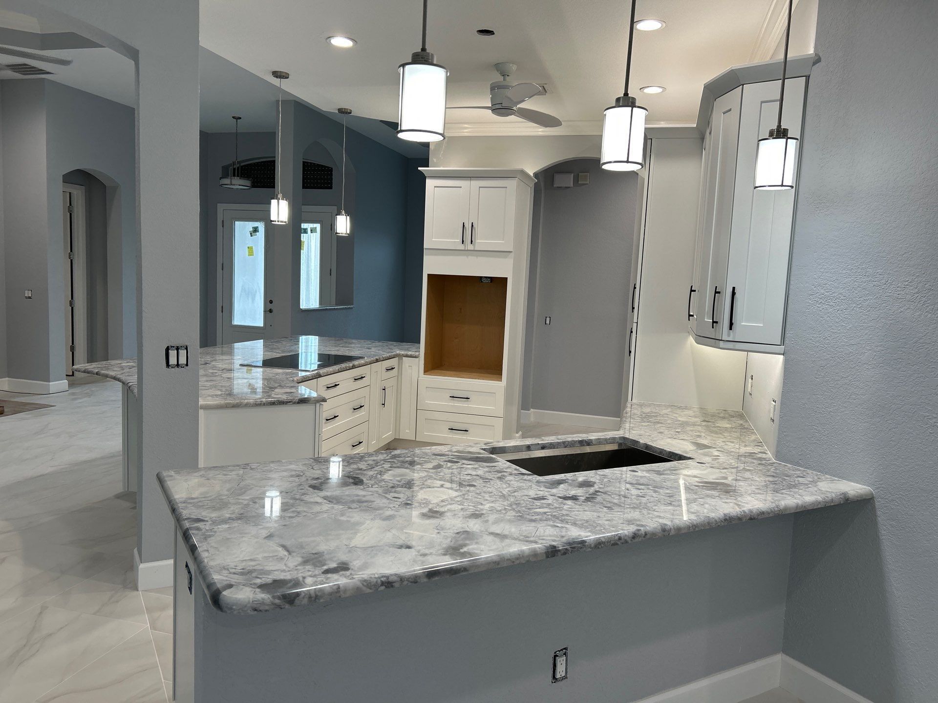 Bright modern kitchen with gray cabinets, white appliances, marble island, and pendant lights