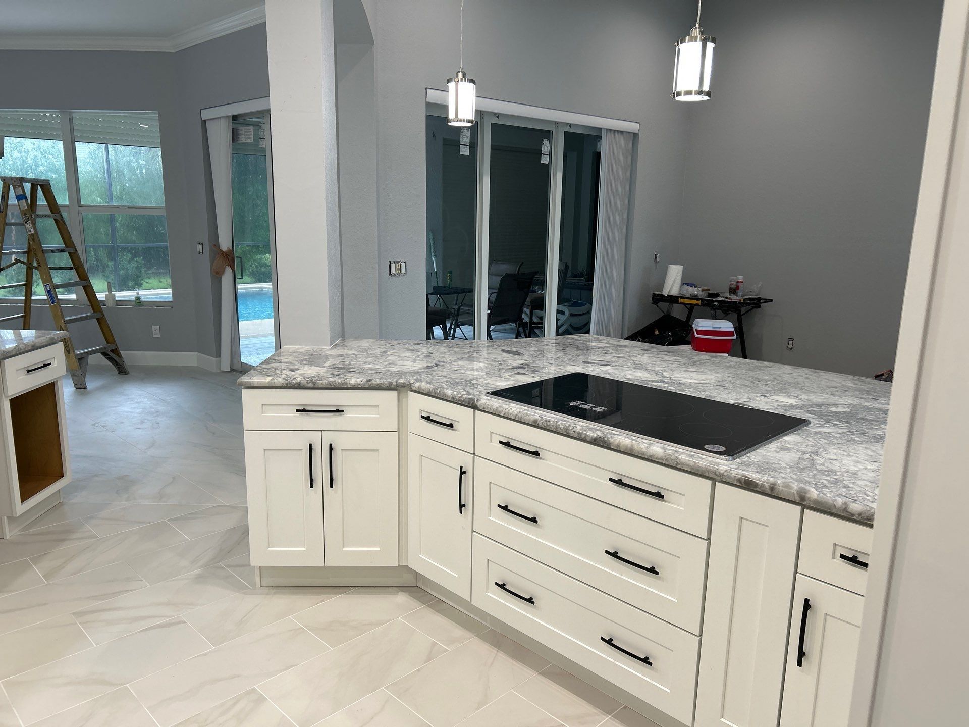Modern kitchen with white cabinets, gray granite island, pendant lights, and sliding glass doors.