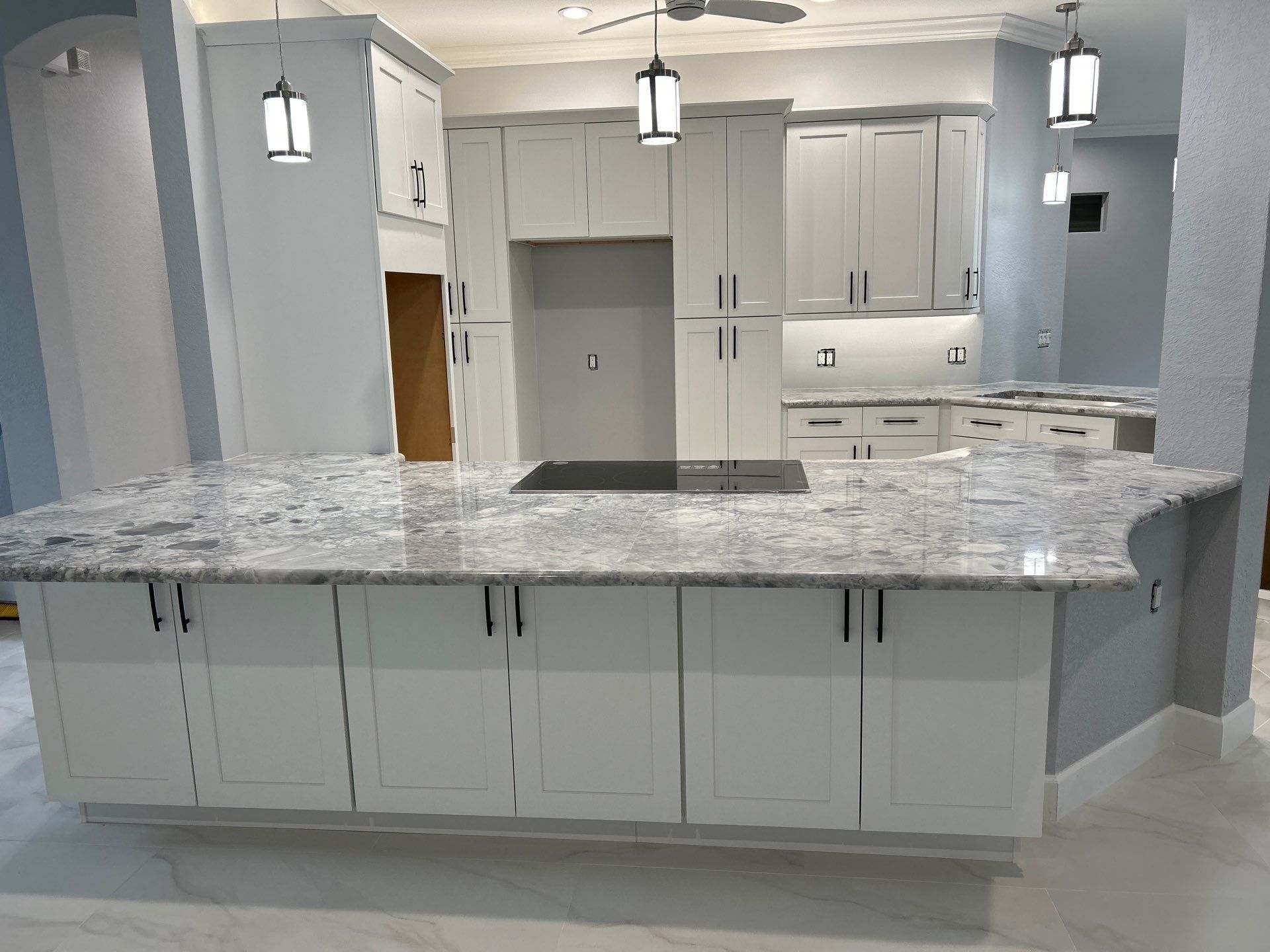 Spacious modern kitchen with white cabinets, gray granite island, and pendant lights