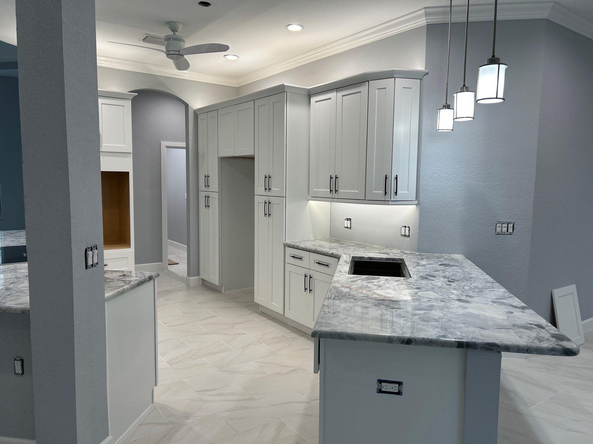 Modern kitchen with gray cabinets, marble island, pendant lights, and light tile flooring