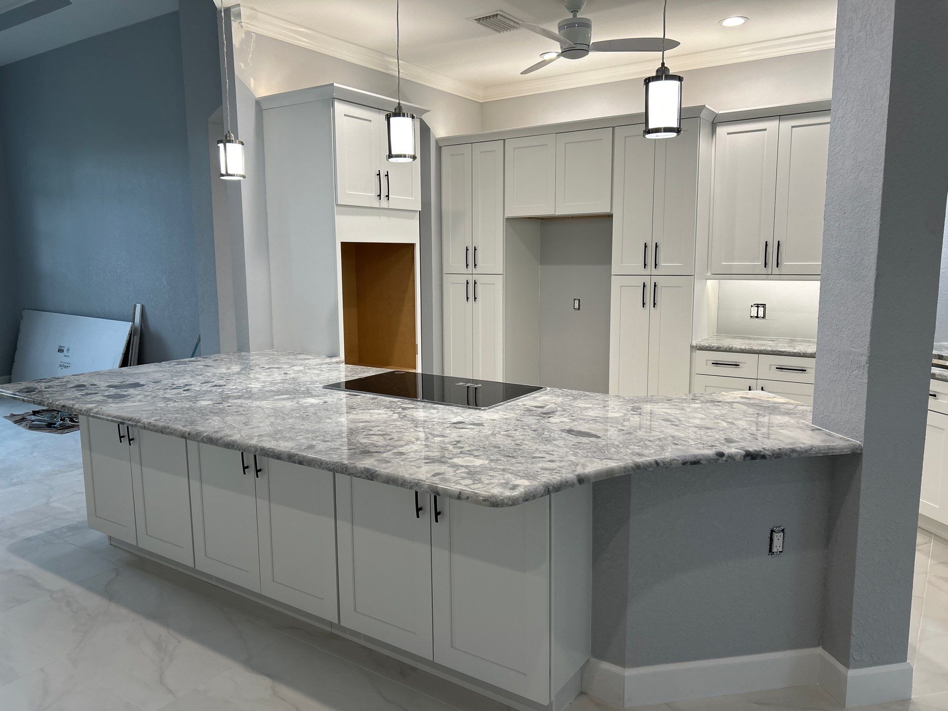 Modern white kitchen with gray island, granite countertops, and pendant lights