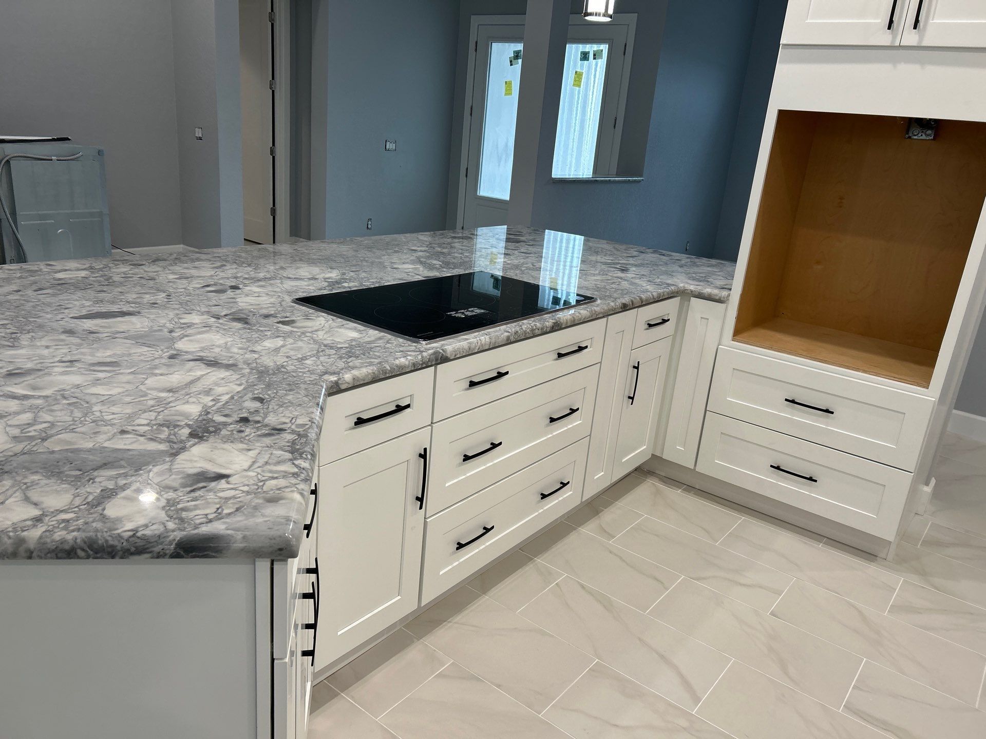 Kitchen with gray granite island, cream cabinets, and a stainless sink in a bright tiled room