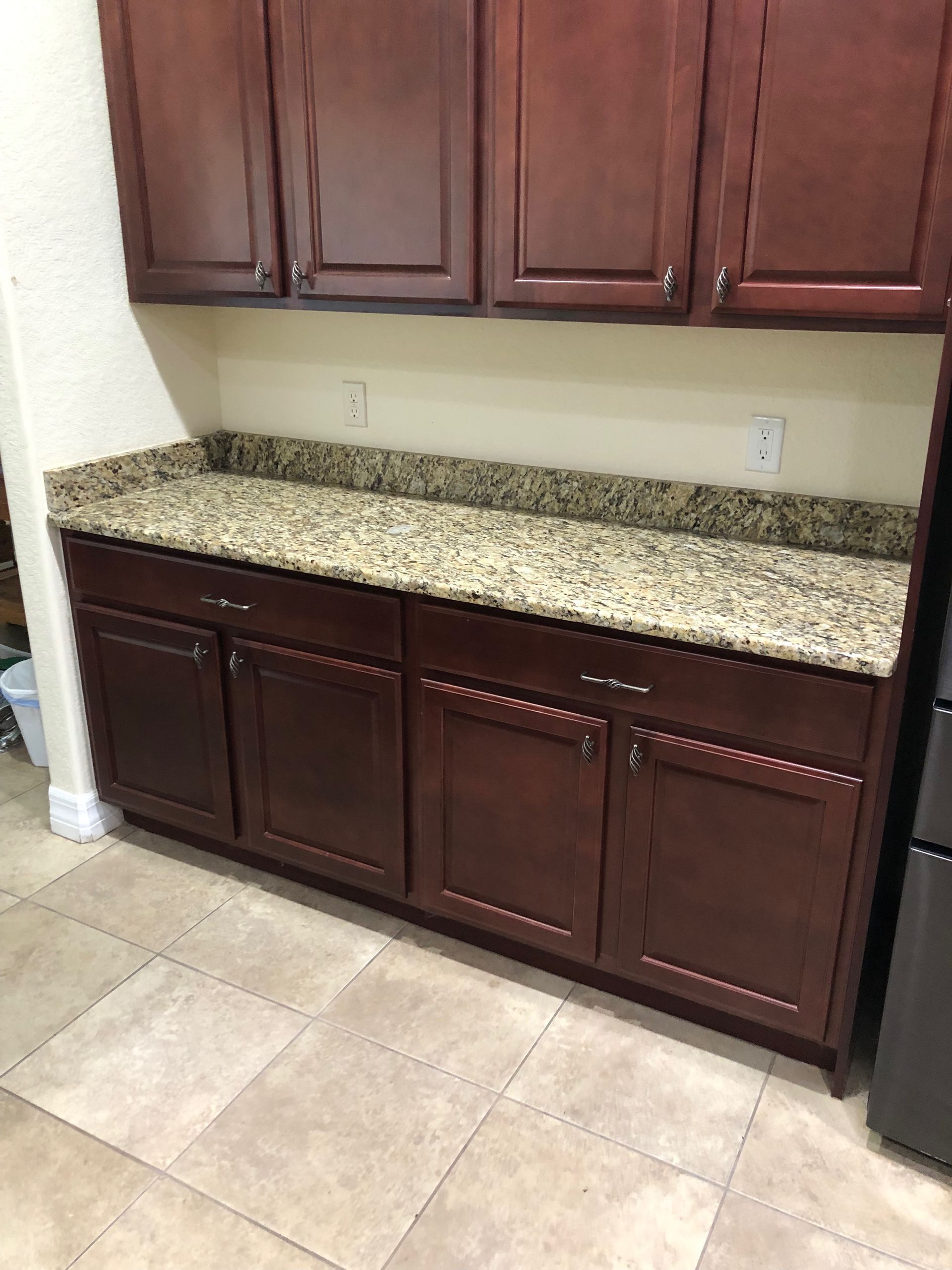 Dark wood kitchen cabinets with granite countertop and beige tile floor against a wall