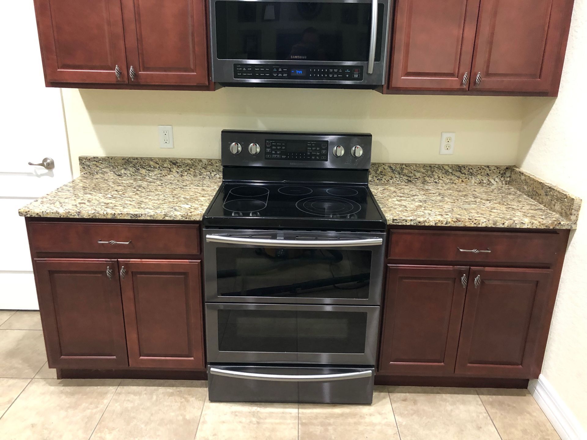 Kitchen with dark wood cabinets, granite countertops, and a stainless steel oven below a microwave.