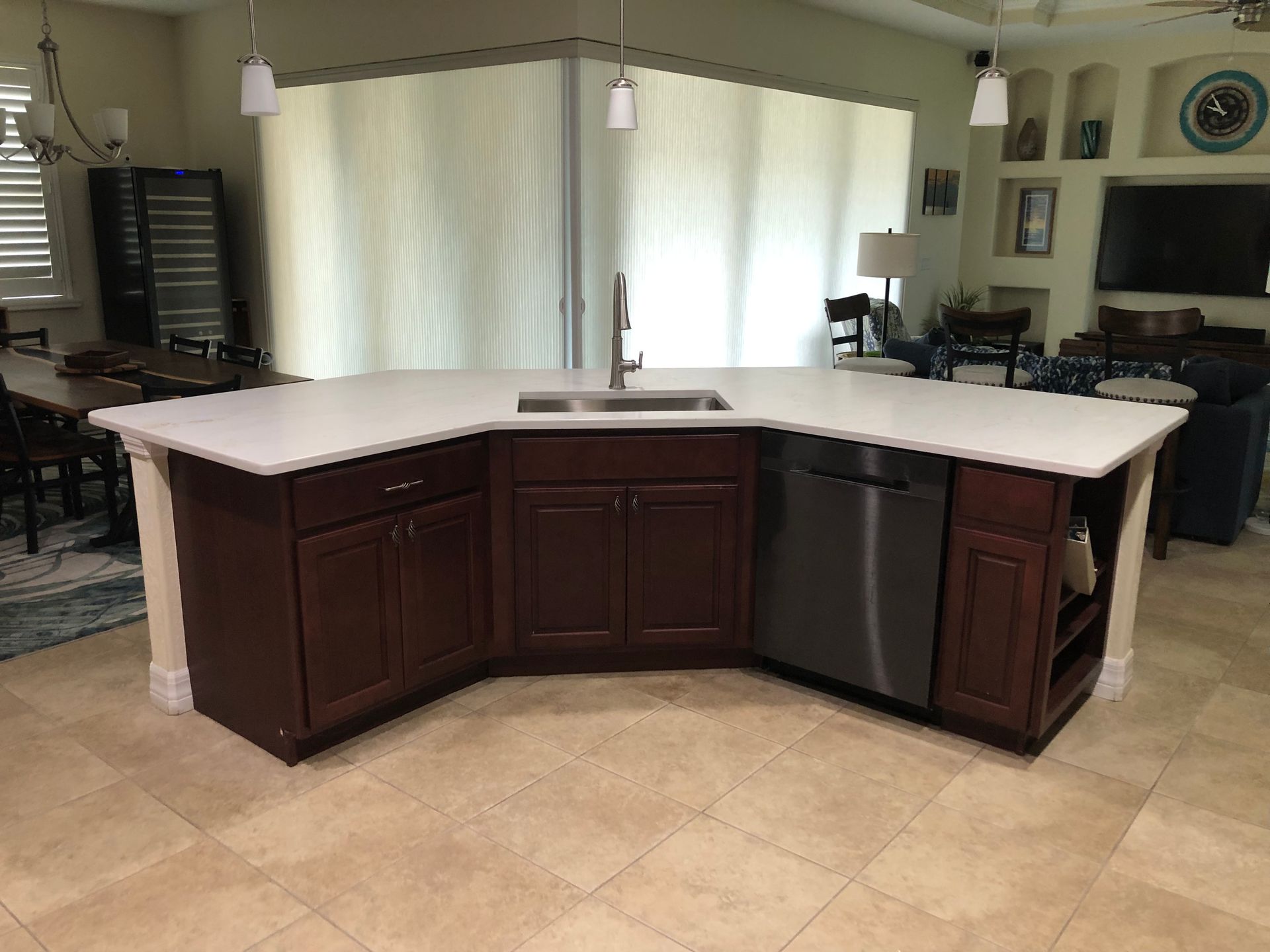 Kitchen island with dark wood cabinets, white countertop, and stainless-steel sink in a tiled room.