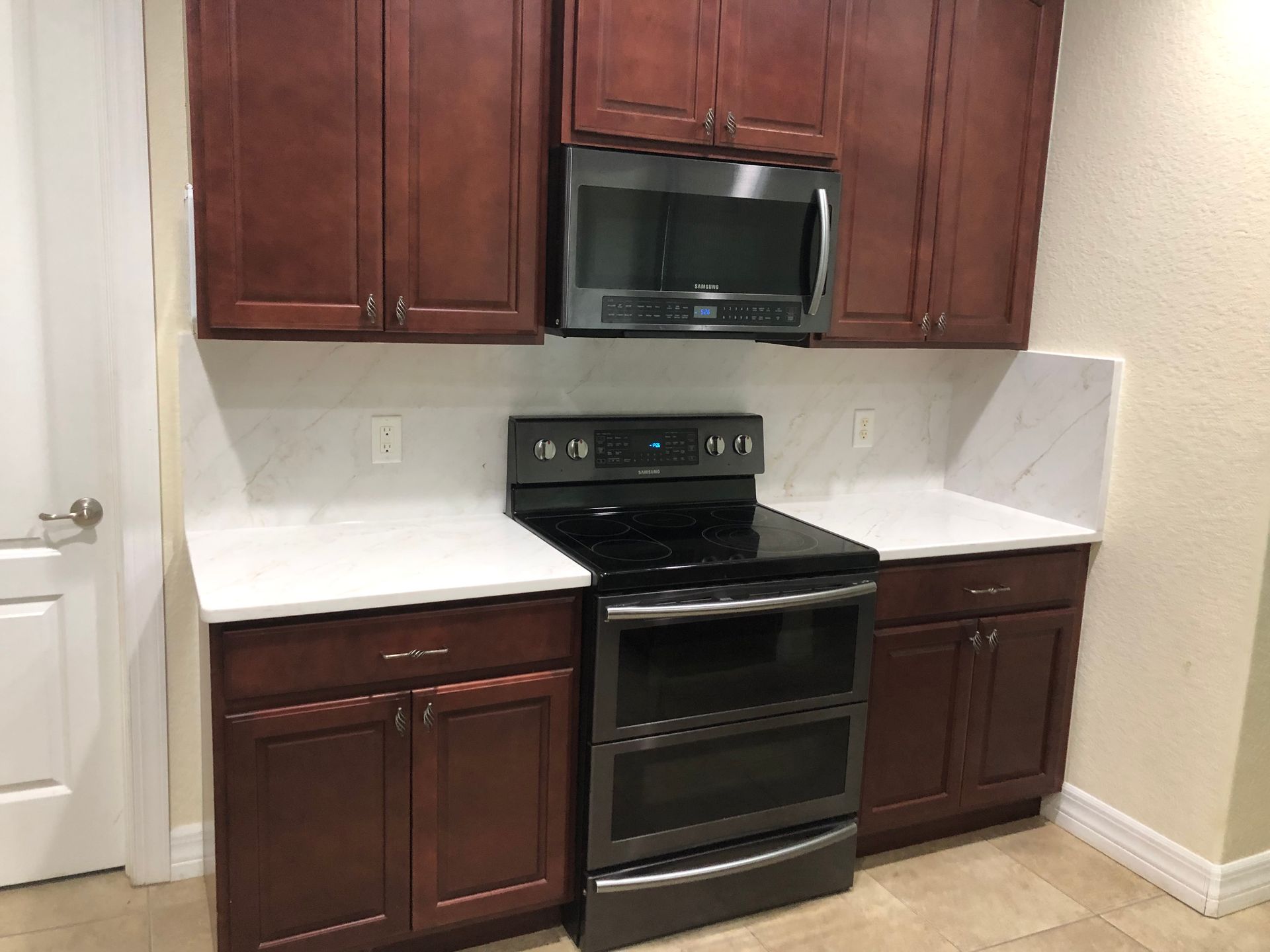 Compact kitchen nook with dark wood cabinets, white counters, and a black stove and microwave