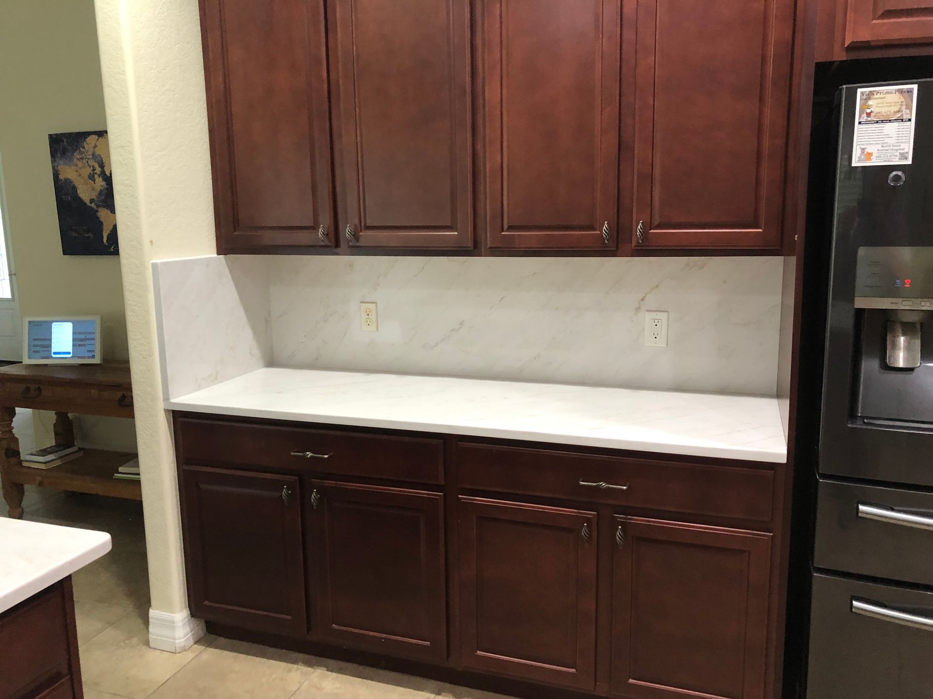 Kitchen cabinets and white countertop beside a stainless-steel refrigerator in a kitchen.
