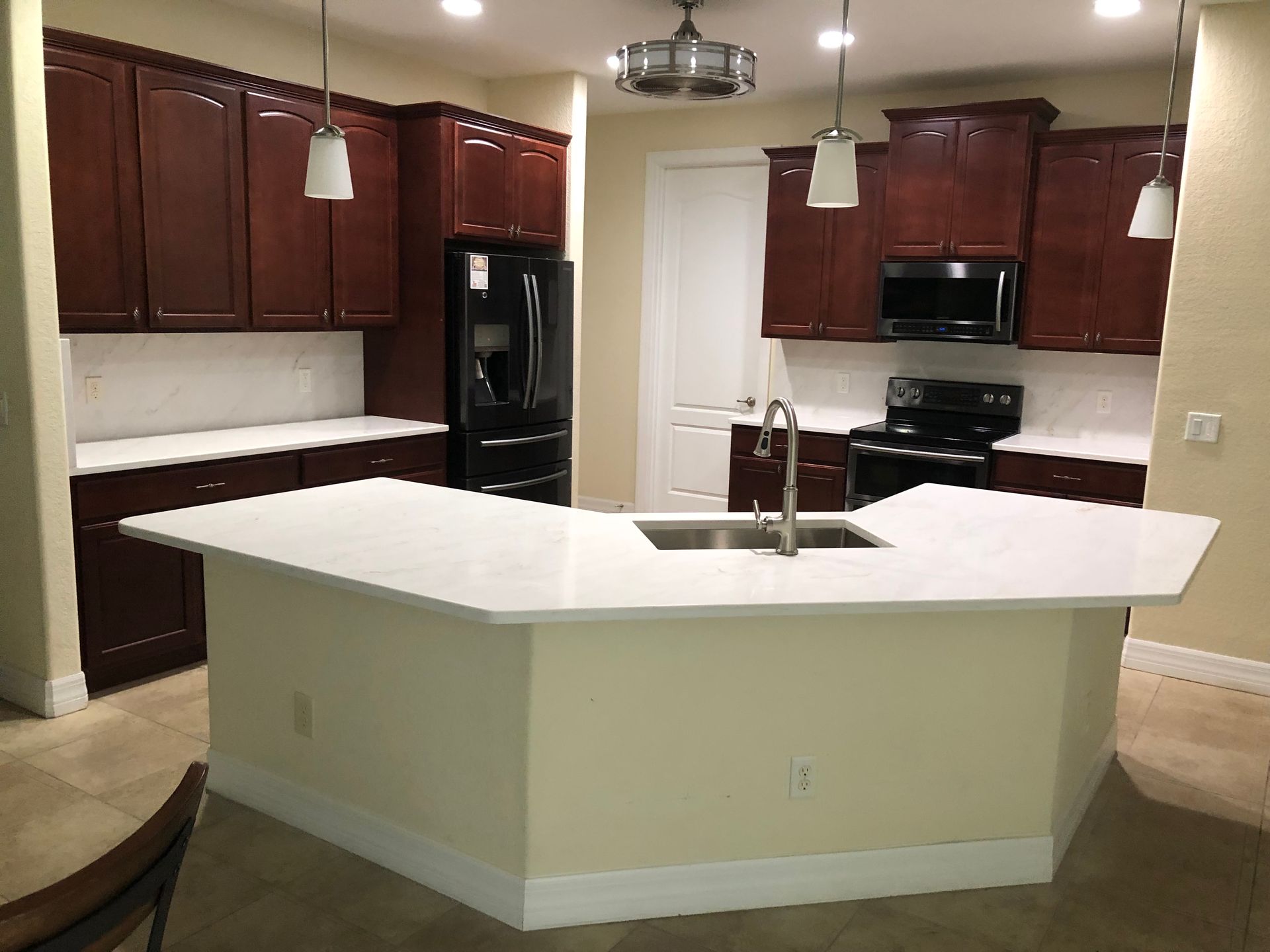 Modern kitchen with dark wood cabinets, white island countertop, black appliances, and pendant lights