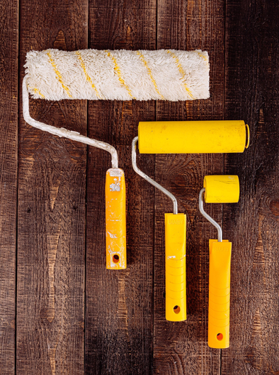 Four yellow paint rollers and one white roller head on a wooden background