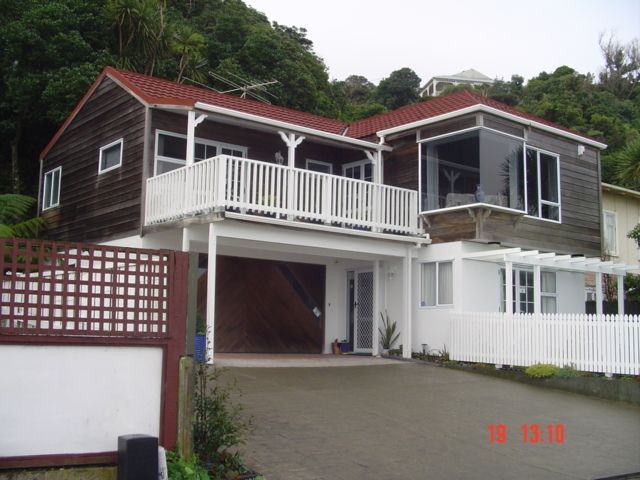 Two-story house with brown siding, white railings, and red roof, on a sloped driveway.