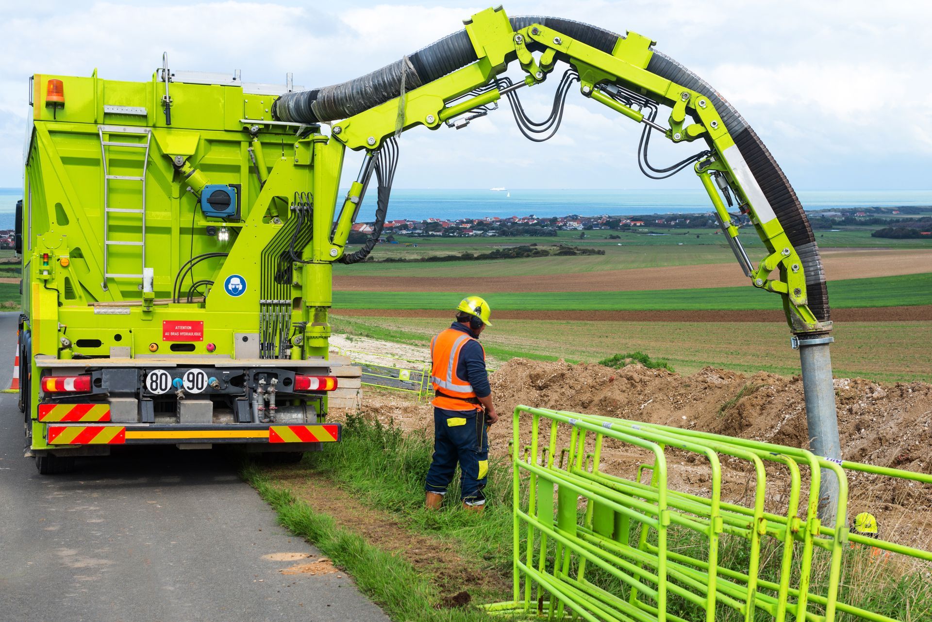 Industrial vacuum excavation truck with boom arm deployed at an outdoor excavation site with worker 