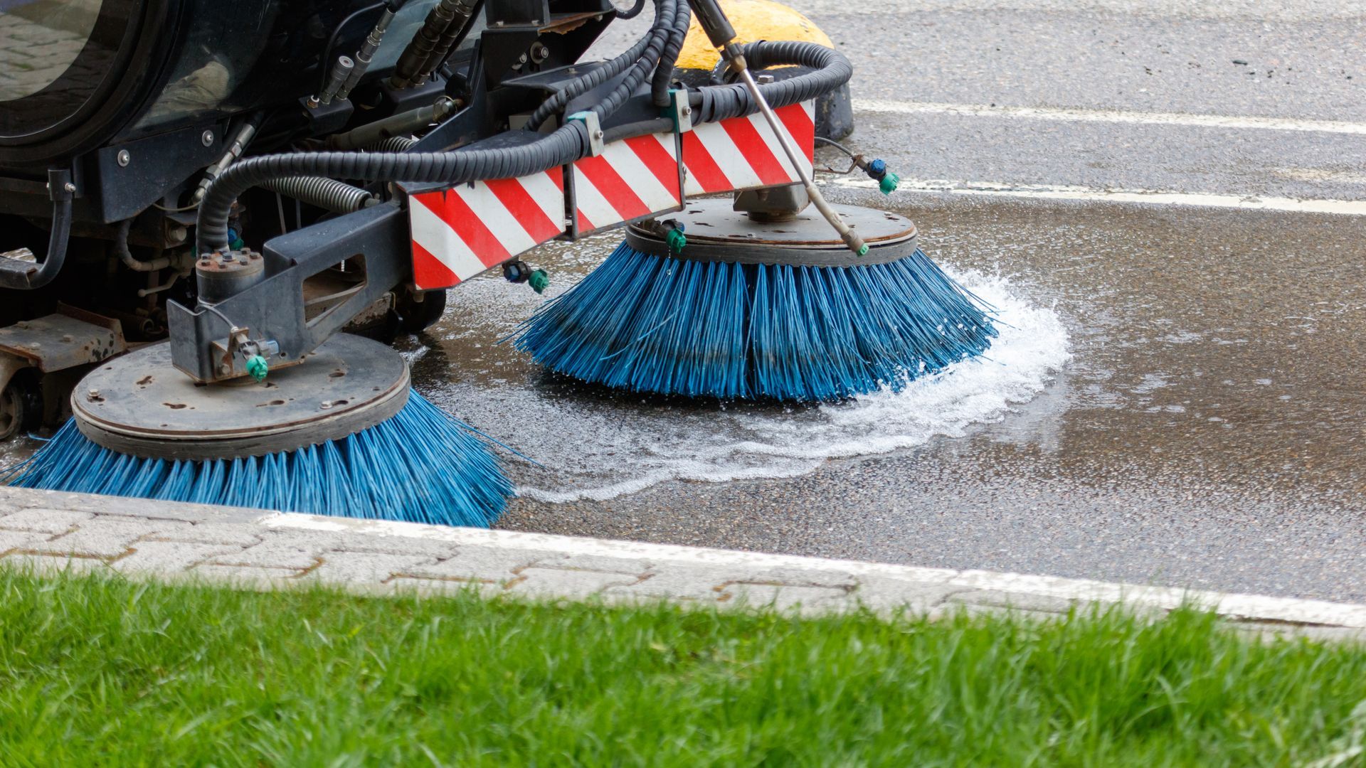 Vacuum truck services cleaning street with rotating brushes and water spray on asphalt surface.