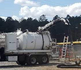 Person in work clothes power washing a white roof.