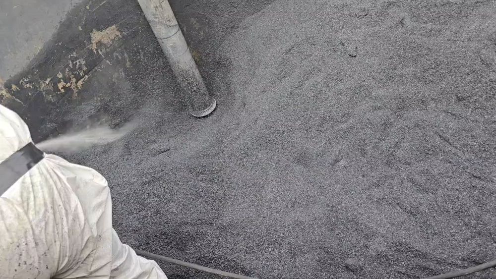 Technician in protective suit using an industrial vacuum hose to remove sludge and waste
