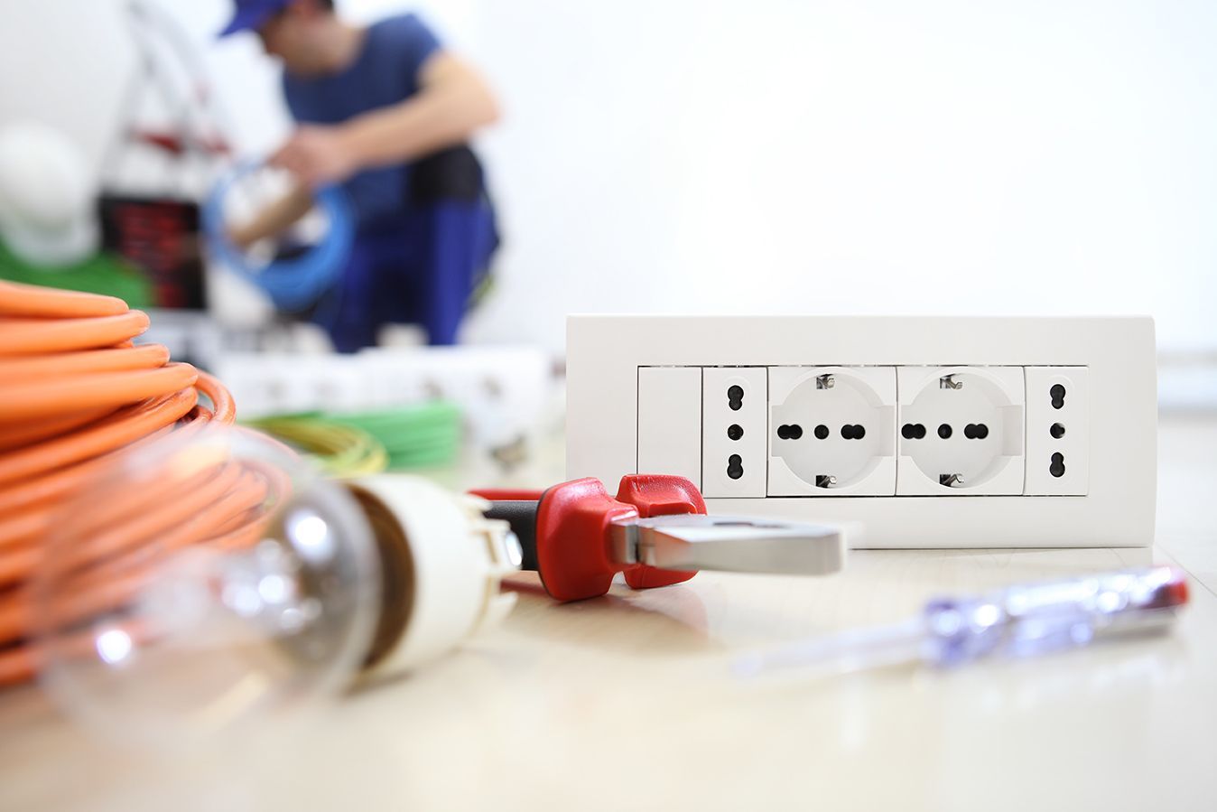 Elettricista che lavora al cablaggio con prese elettriche e utensili in primo piano.