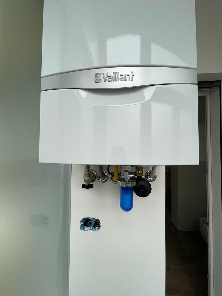 Caldaia Vaillant bianca montata a parete con tubi e filtro per l'acqua blu.
