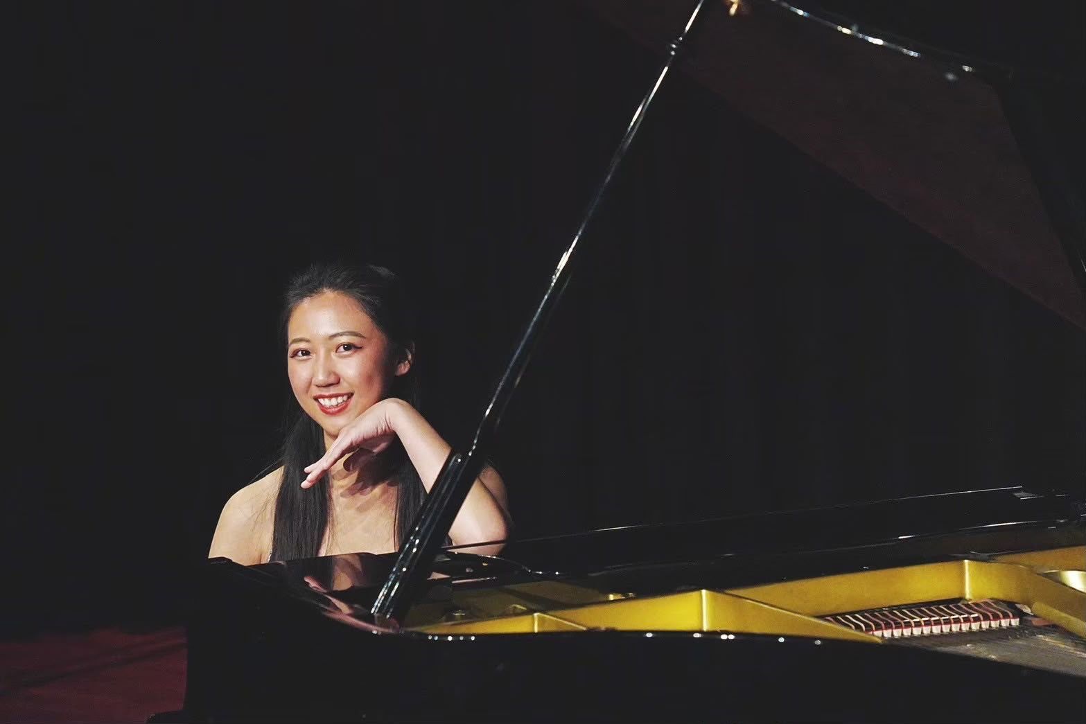 Een pianodocent uit Utrecht glimlacht naar een vleugel op een donker podium met open klep.