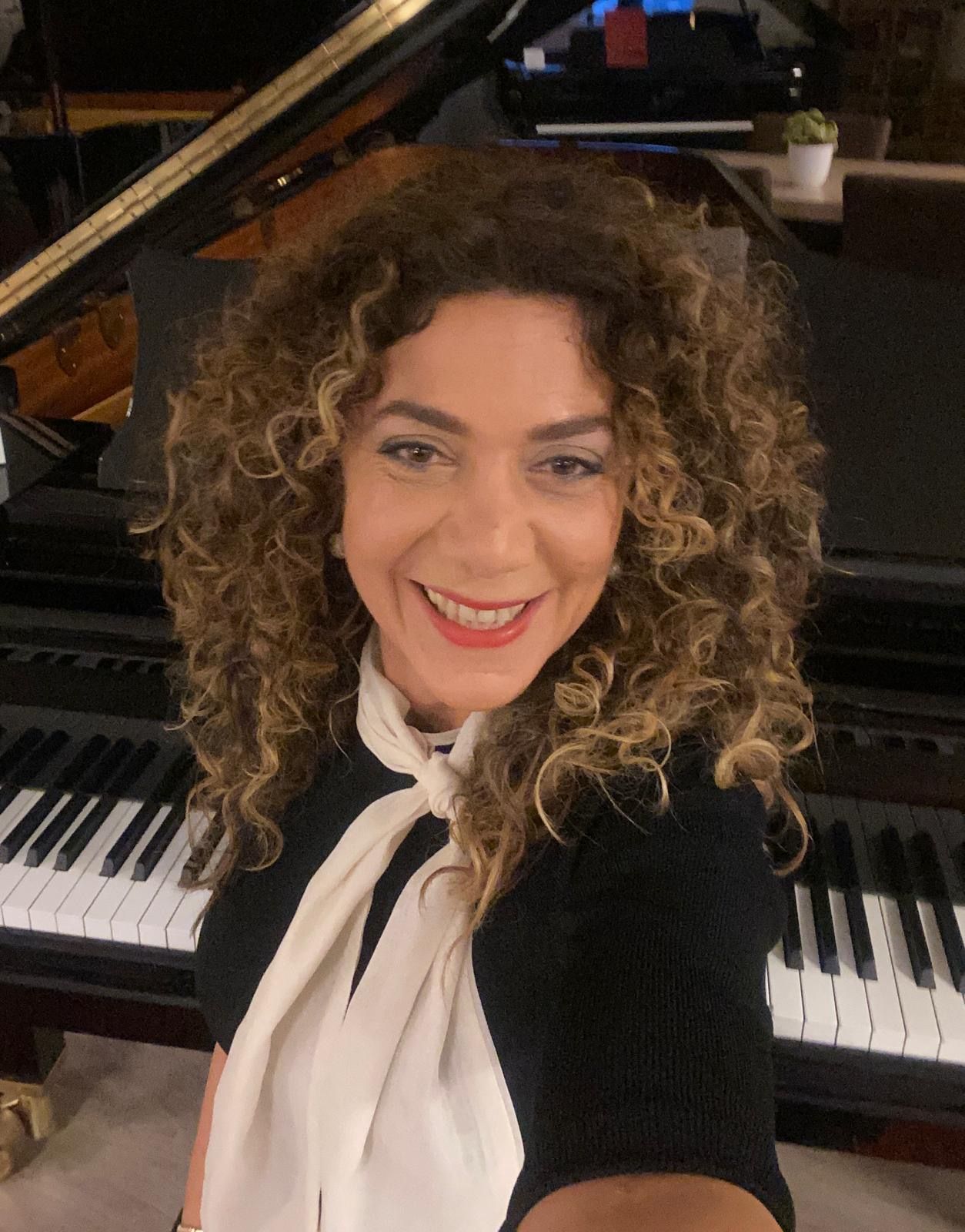 Pianodocent Ceylan Merdol uit Rotterdam in een zwart-wit outfit zit aan een piano in een schemerige kamer.