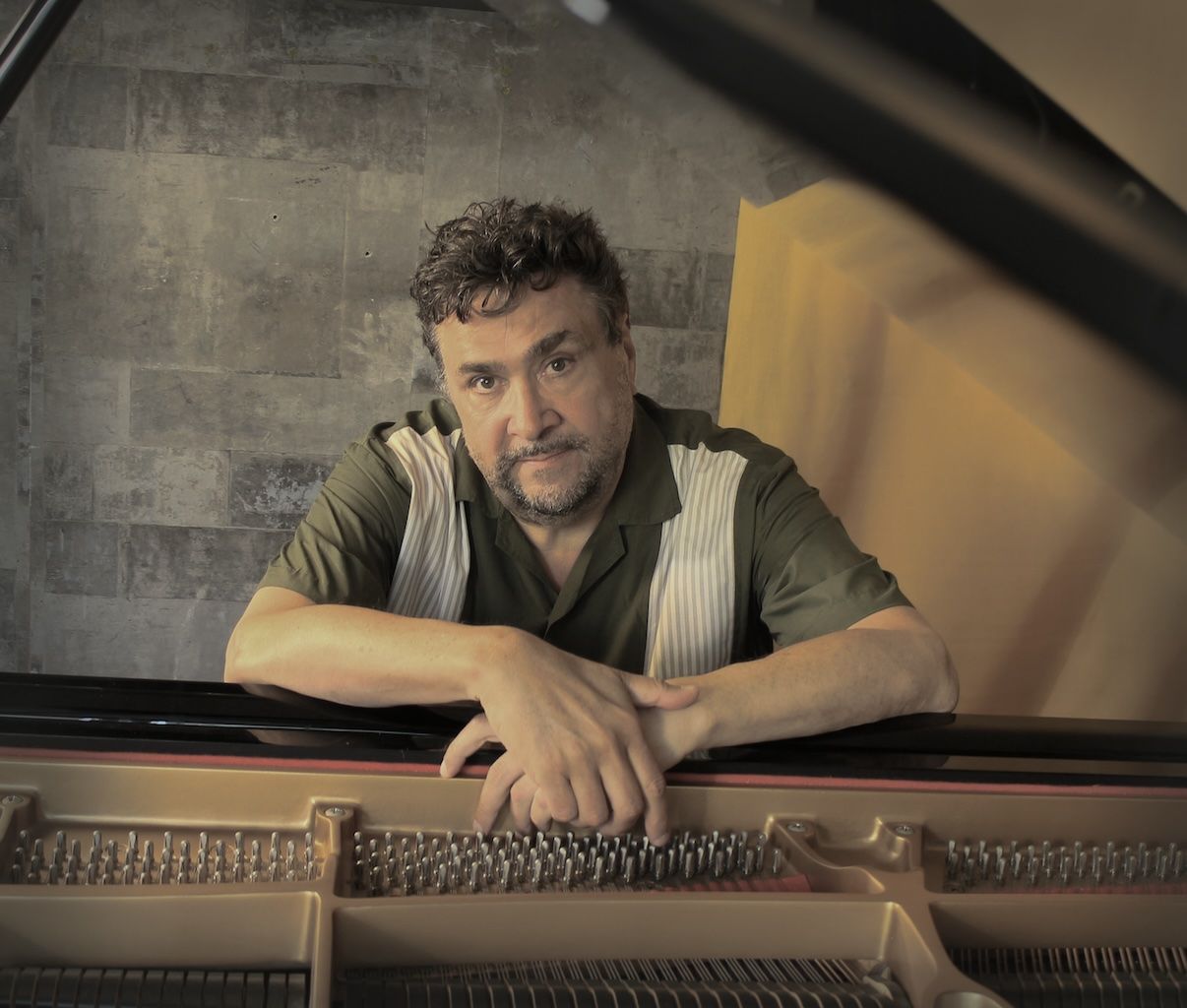 Pianodocent Marcel Moek buigt zich over een piano en kijkt peinzend naar beneden in een schemerige studio.