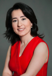 Pianodocent Anna Yedigaryan uit Haarlem in een rode mouwloze jurk, lachend tegen een grijze studioachtergrond.