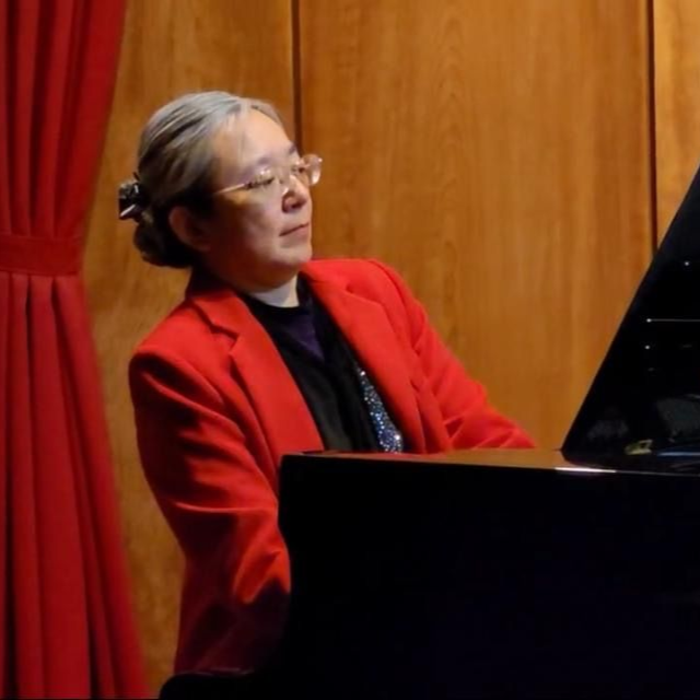 Pianodocent Grace Hsu uit Almere in een rode jas speelt op een vleugel op een podium met rode gordijnen.
