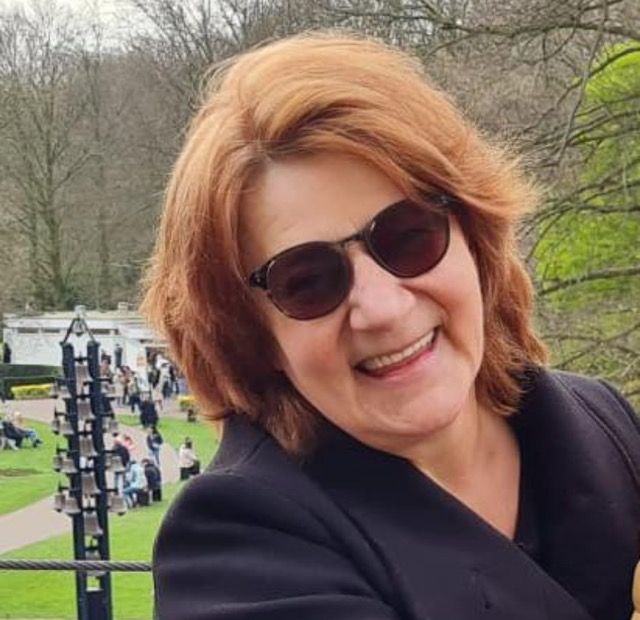 Vanja Marinova, pianodocent uit Zaandam en Amsterdam  met een zonnebril en roodbruin haar, gekleed in een zwarte jas, bevindt zich buiten in een park.
