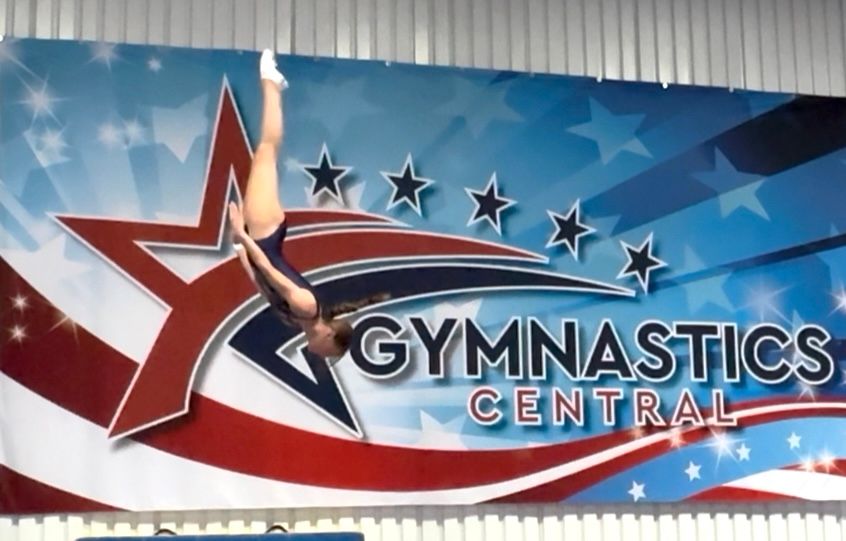 A young girl is sitting on a balance beam in a gym.