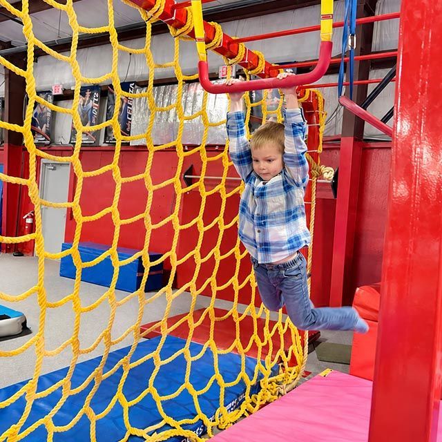A young boy in an orange shirt is climbing a rope