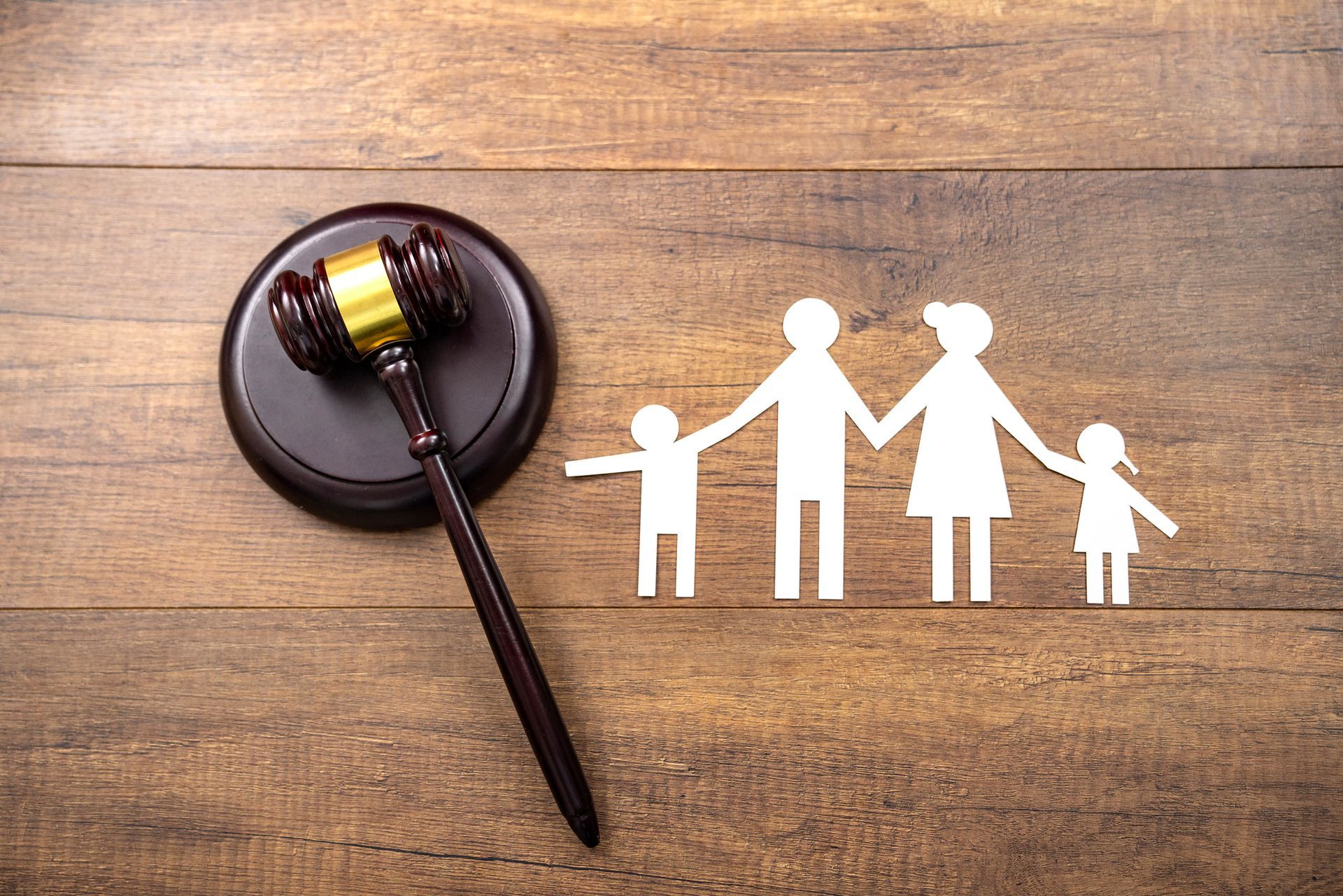 A wooden judge's gavel and a paper cut out of a family on a wooden table.