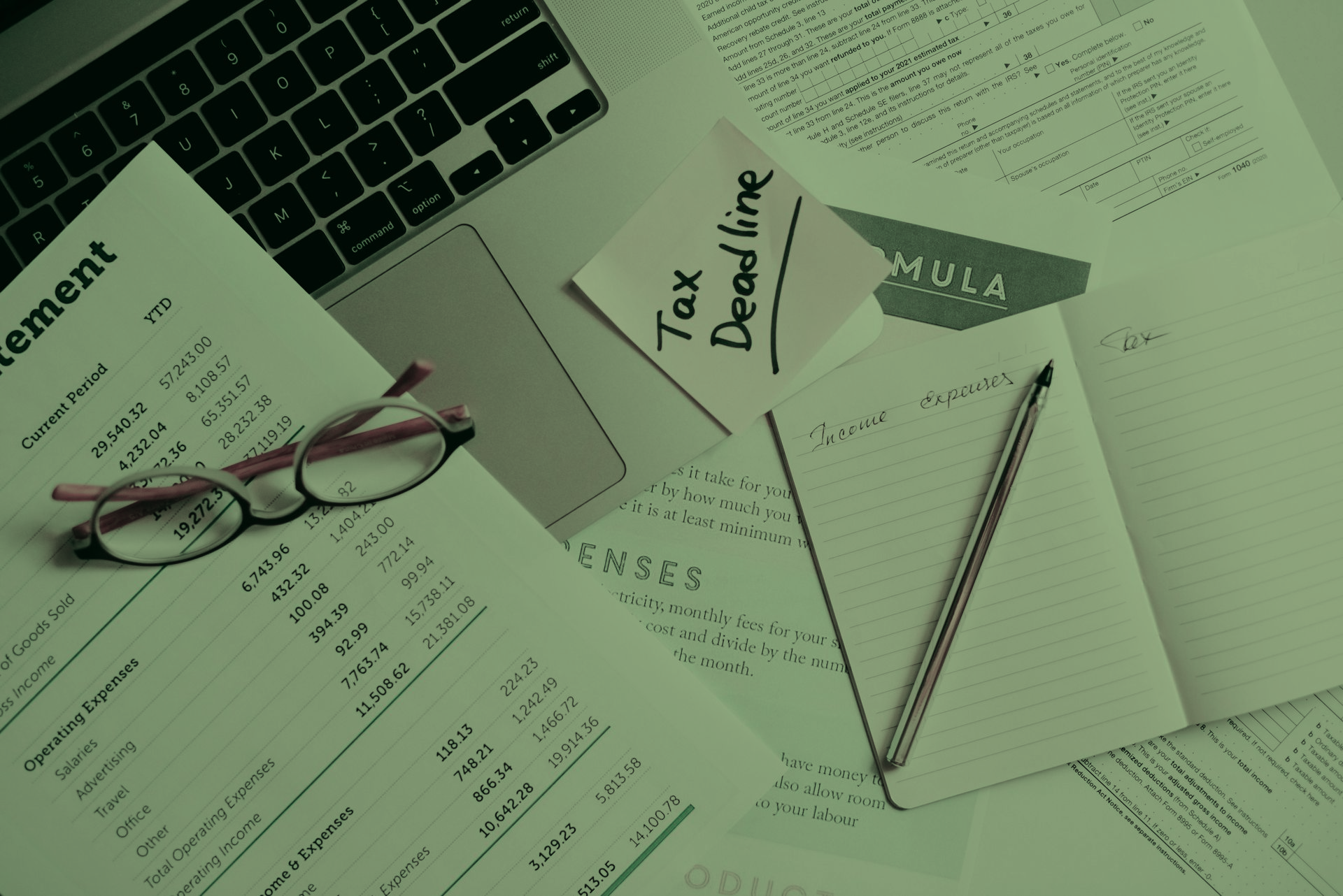 A desk with a laptop , notebooks , papers and a sticky note that says tax deadline