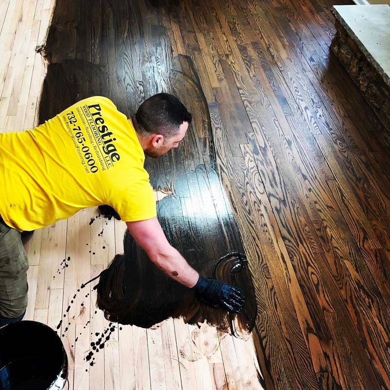 A man wearing a yellow prestige shirt is painting a wooden floor