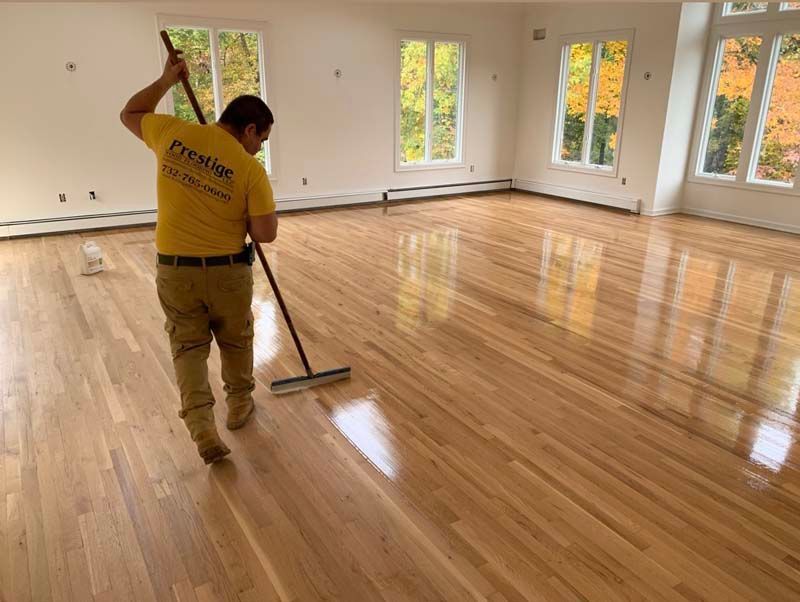 A man in a yellow shirt is cleaning a wooden floor with a mop.
