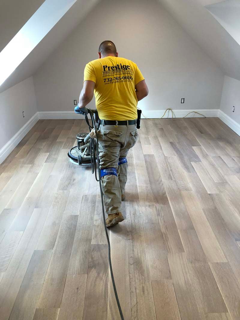 A man in a yellow shirt is sanding a wooden floor with a machine.