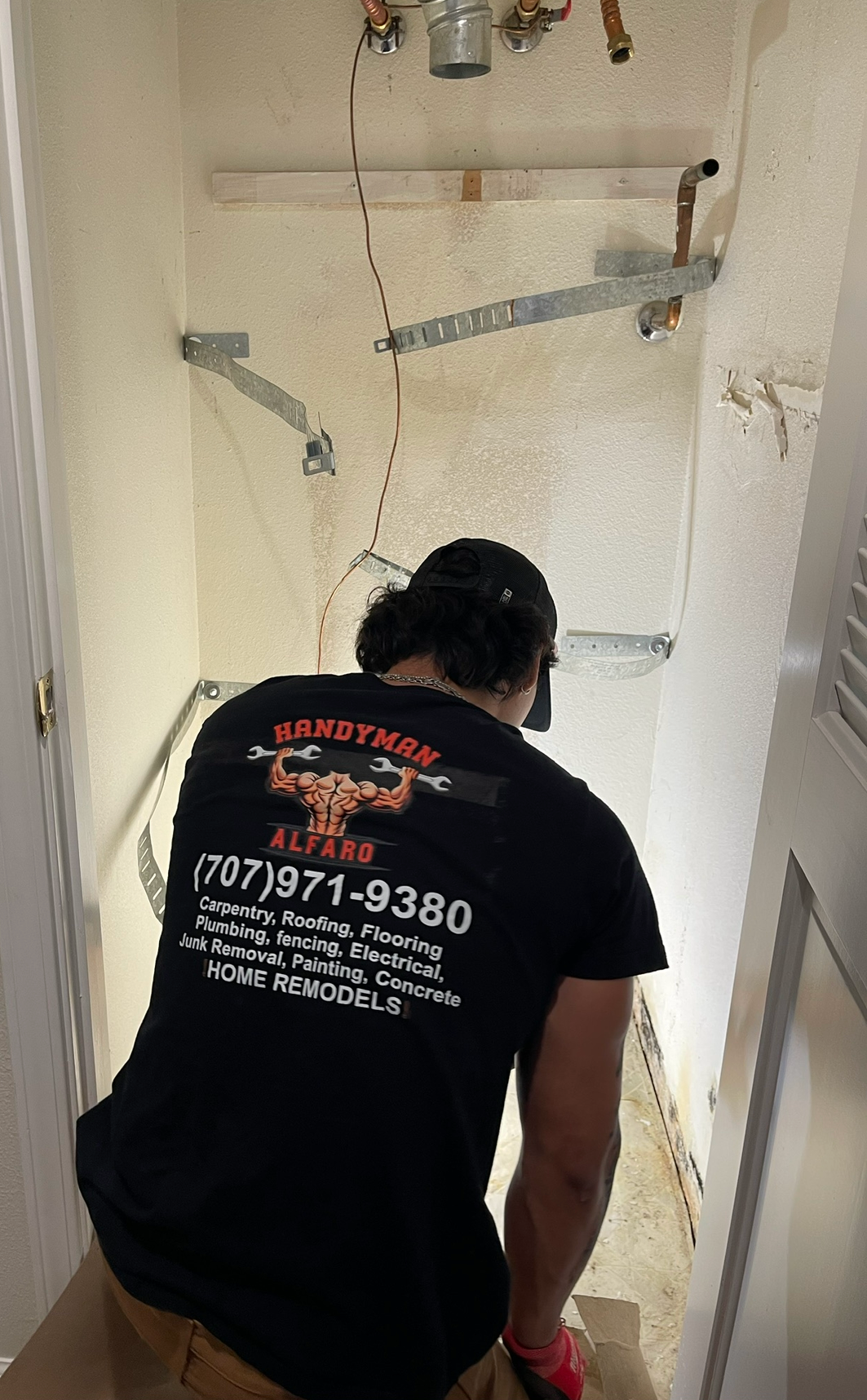 Worker cleaning a shower stall with a hose and scrubber in a small bathroom.