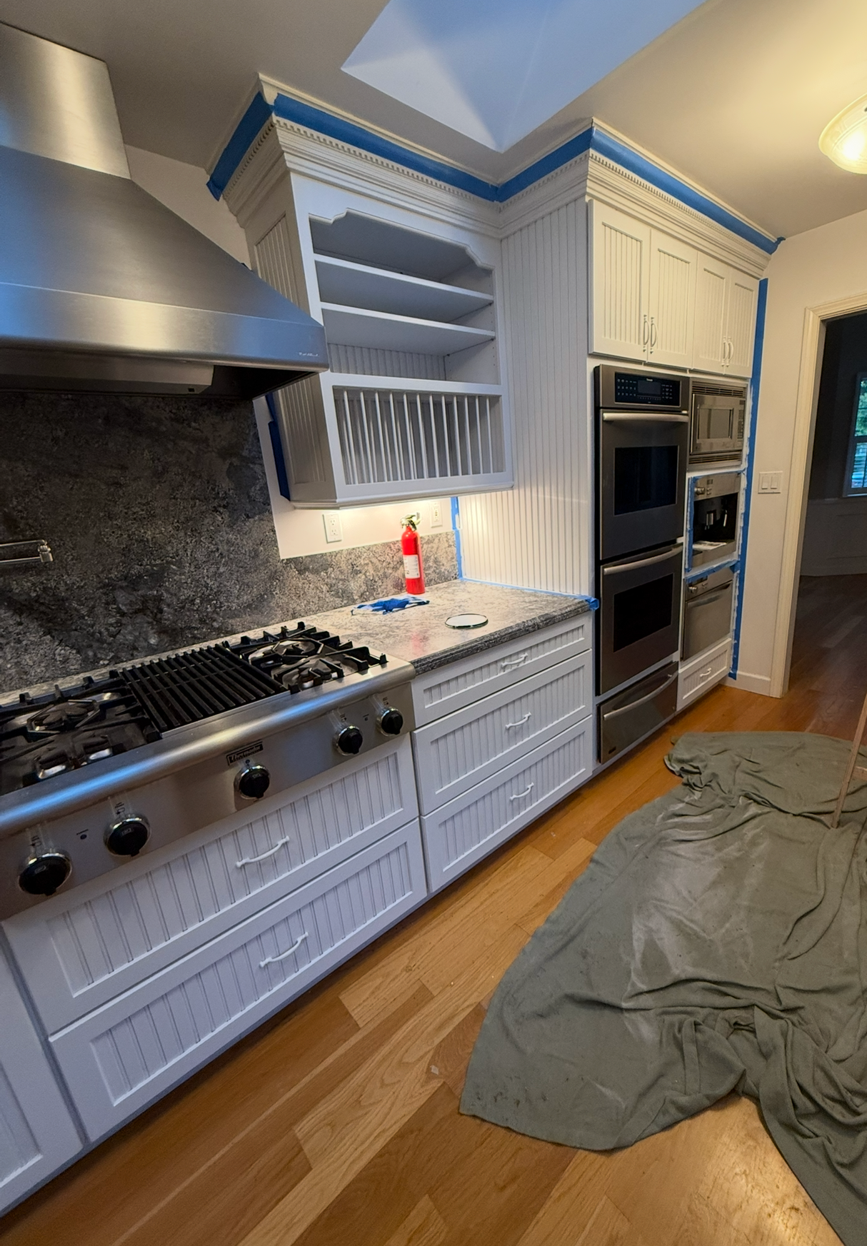 Bright kitchen with stainless stove, white cabinets, blue trim, and a drop cloth on the floor.