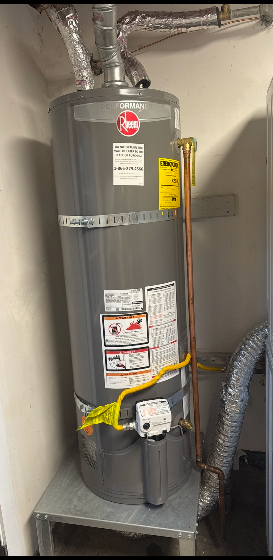 Gray water heater in a utility closet with visible vents, labels, and yellow piping.