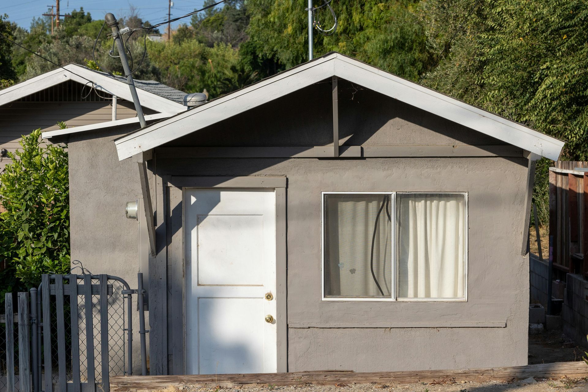 Small gray house with a white door and window behind a metal fence.