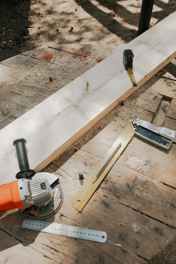 Tools on a wooden plank: angle grinder, ruler, level, and hammer in a workshop setting