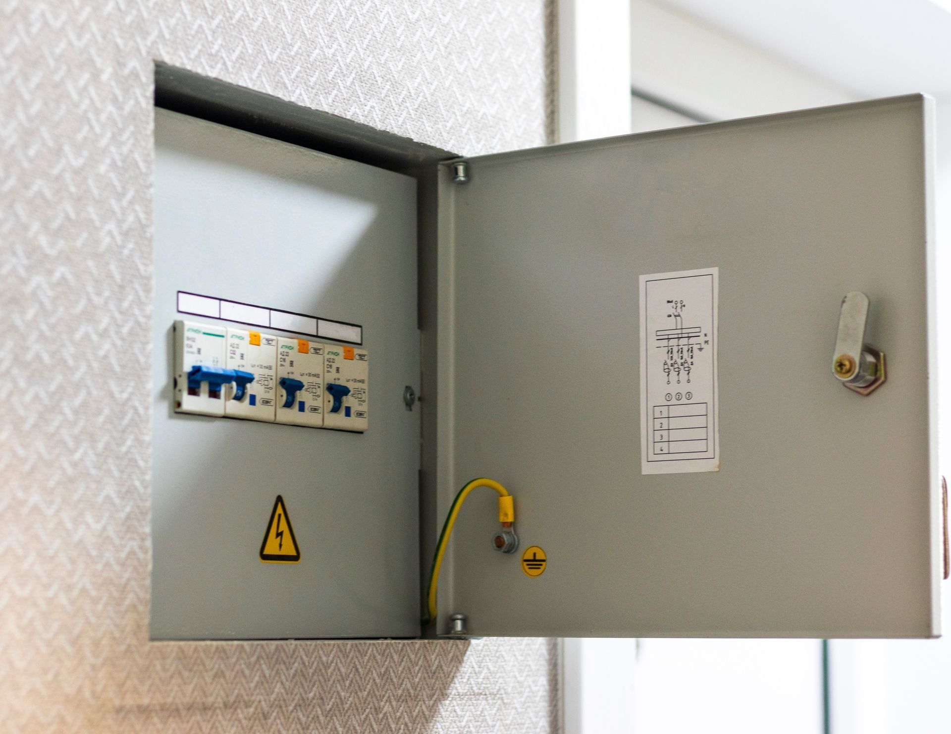 Open electrical breaker panel on a wall, with warning symbol and labeled switches.