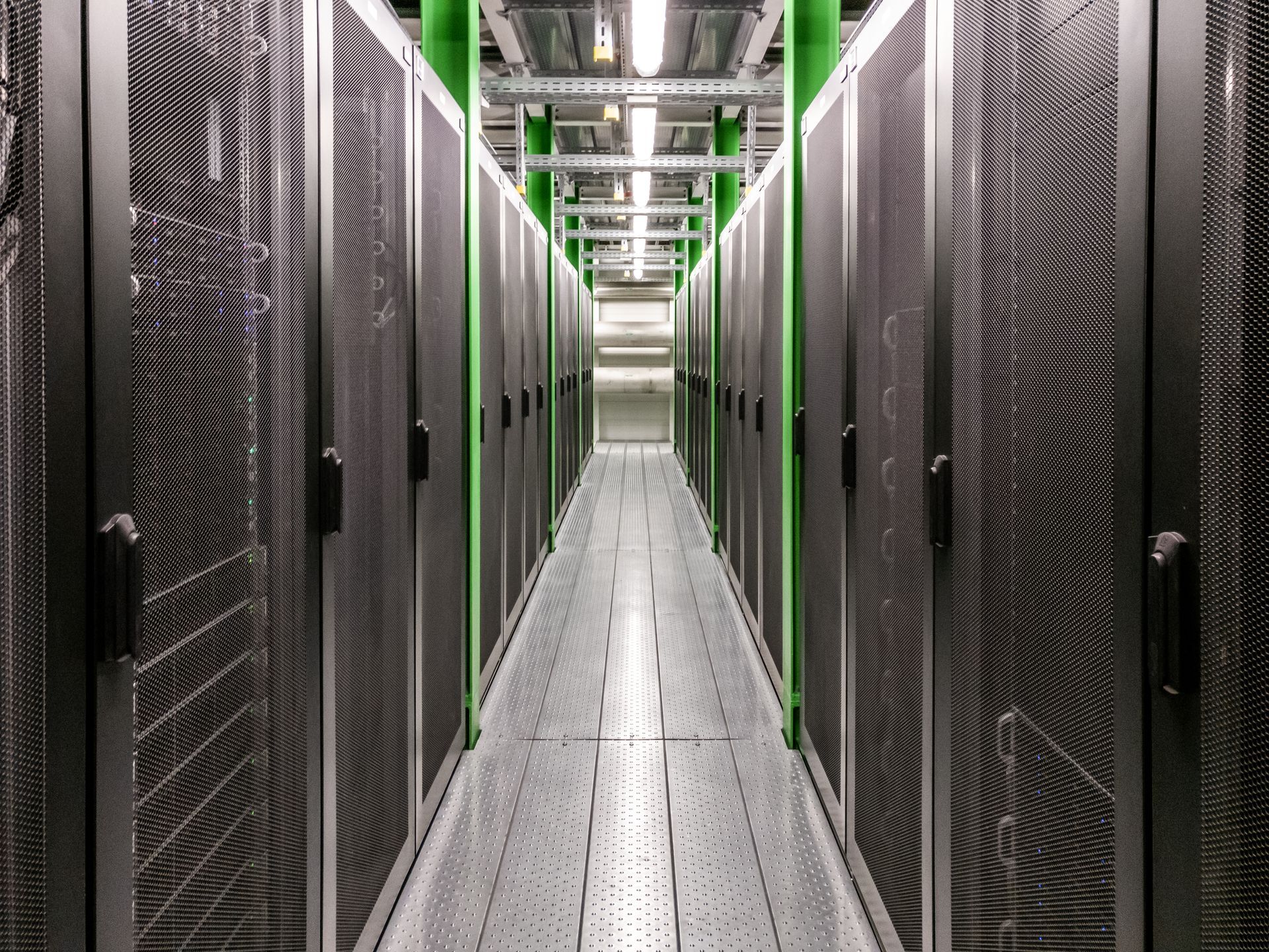 A long server room aisle with rows of black cabinets and bright ceiling lights.