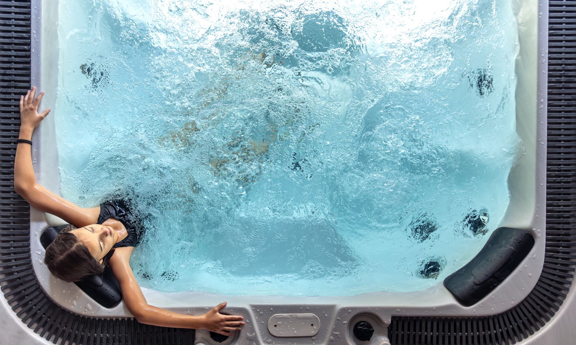 Person relaxing in a hot tub as water jets swirl in a bubbling blue spa
